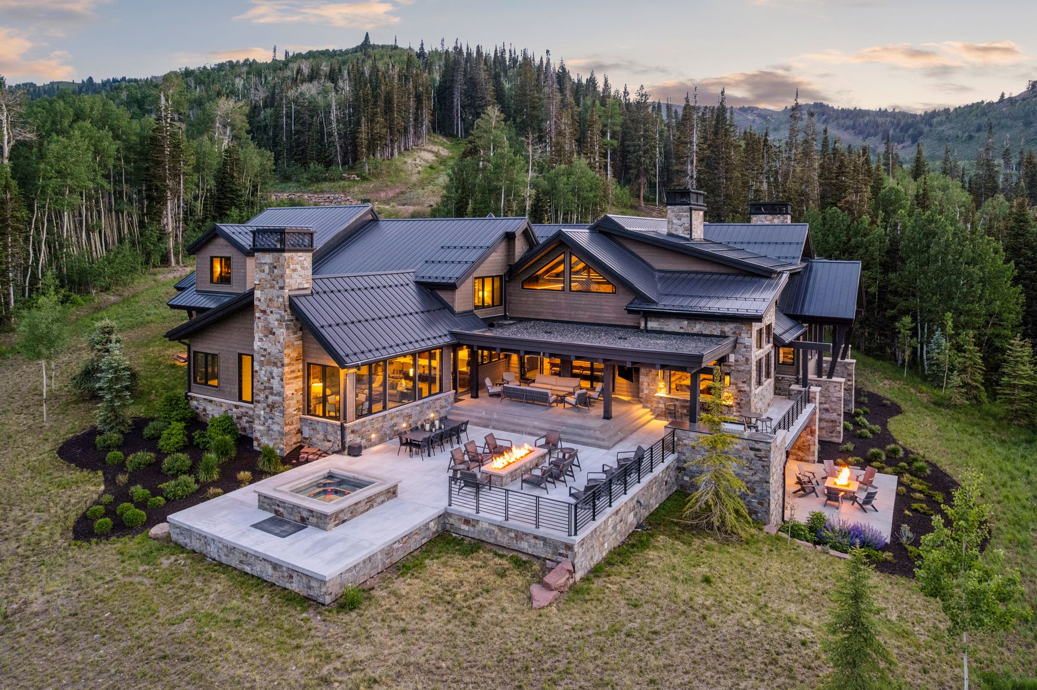 Exterior featuring natural stone and wood siding, a dark metal roof, multiple outdoor patios, and a built-in fire pit