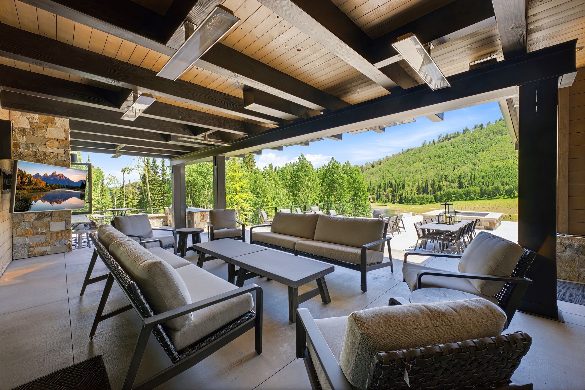 Covered patio featuring a stone-clad pillar, exposed wood beam ceiling with integrated heaters, and a concrete patio floor
