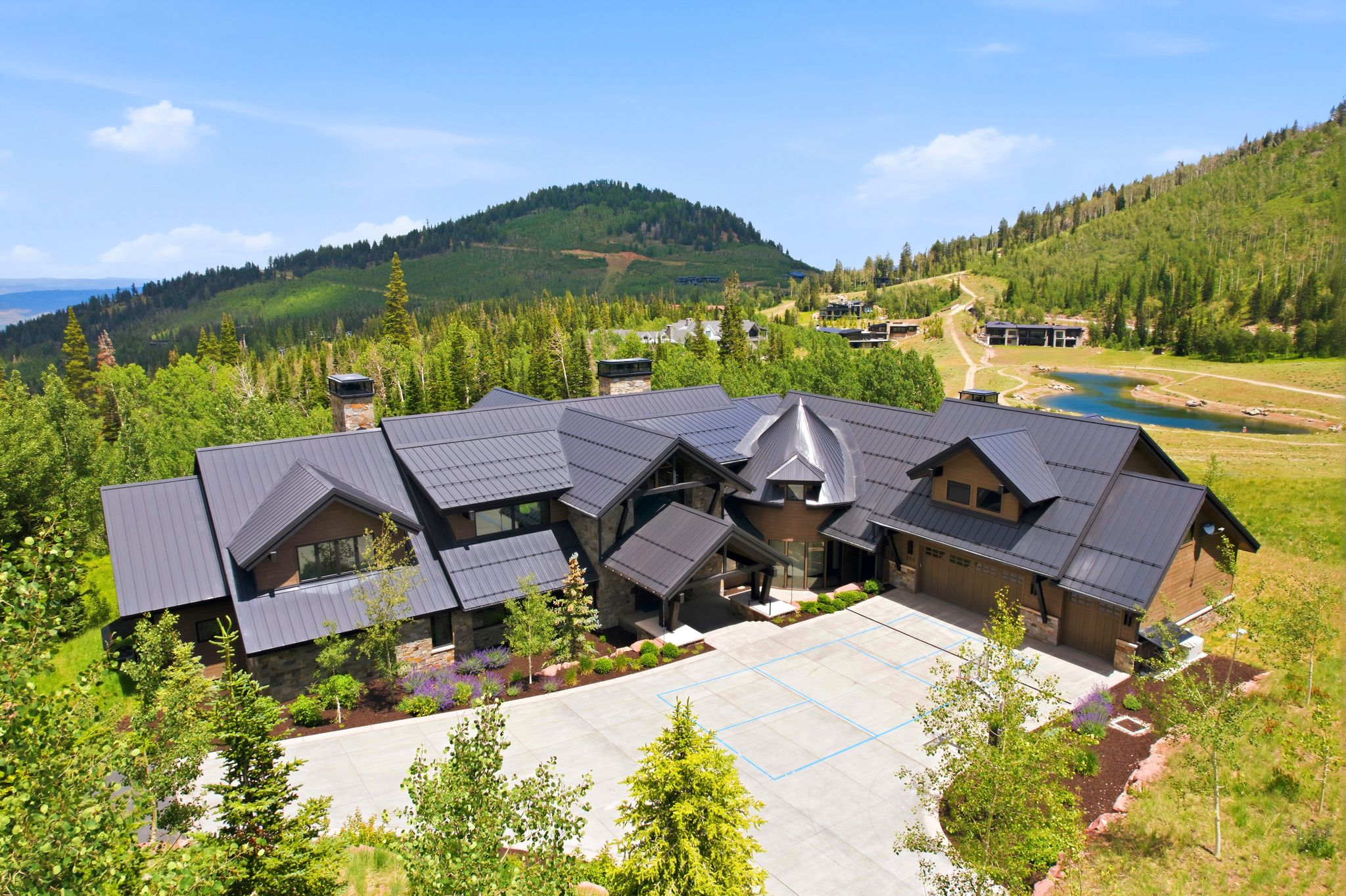 Spacious modern residence featuring a multi-gabled metal roof, stone and wood exterior, and an expansive paved motor court