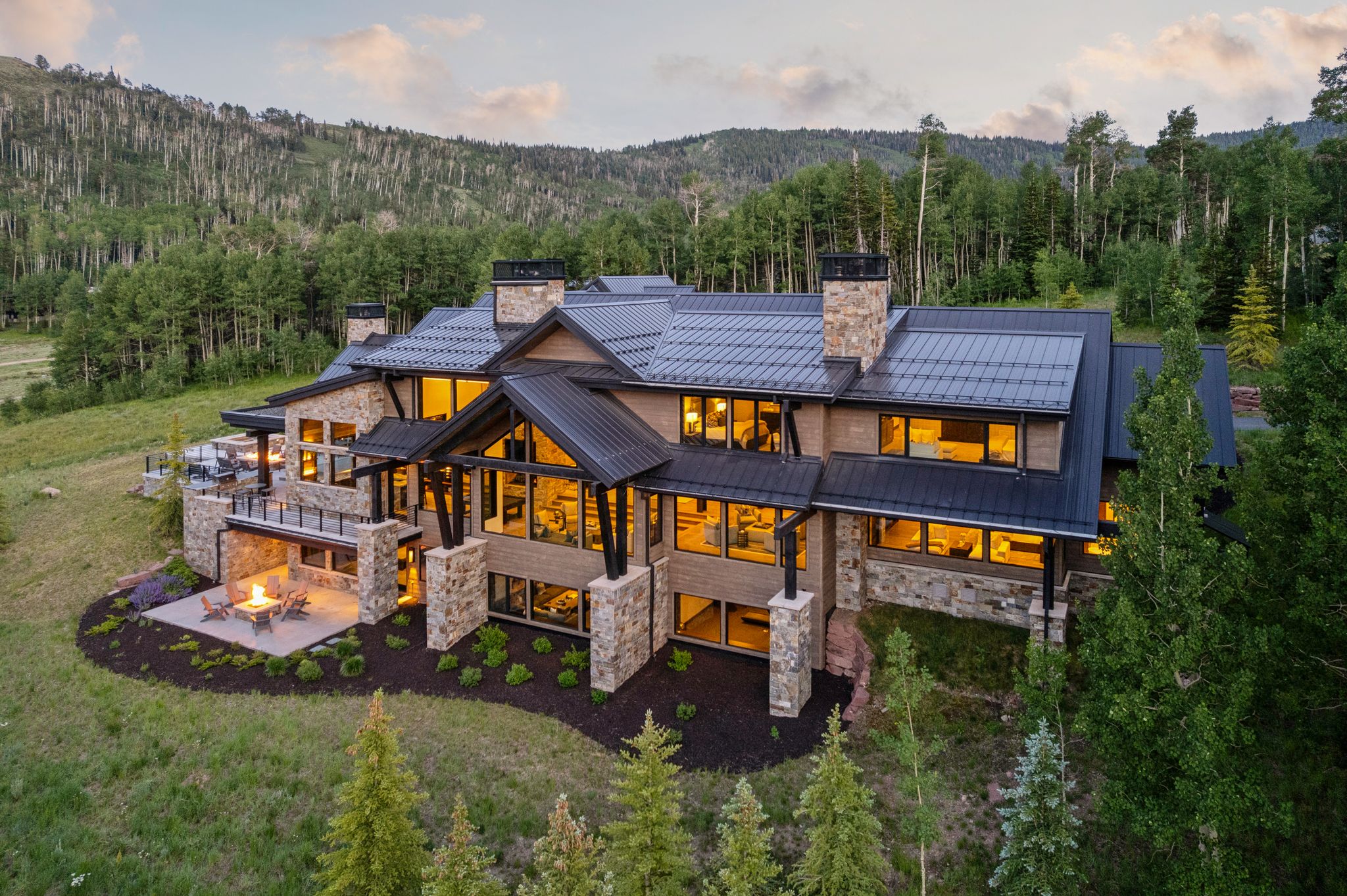 Stone and wood-sided exterior featuring multiple balconies, a lower-level patio with a fire pit, and extensive window arrays