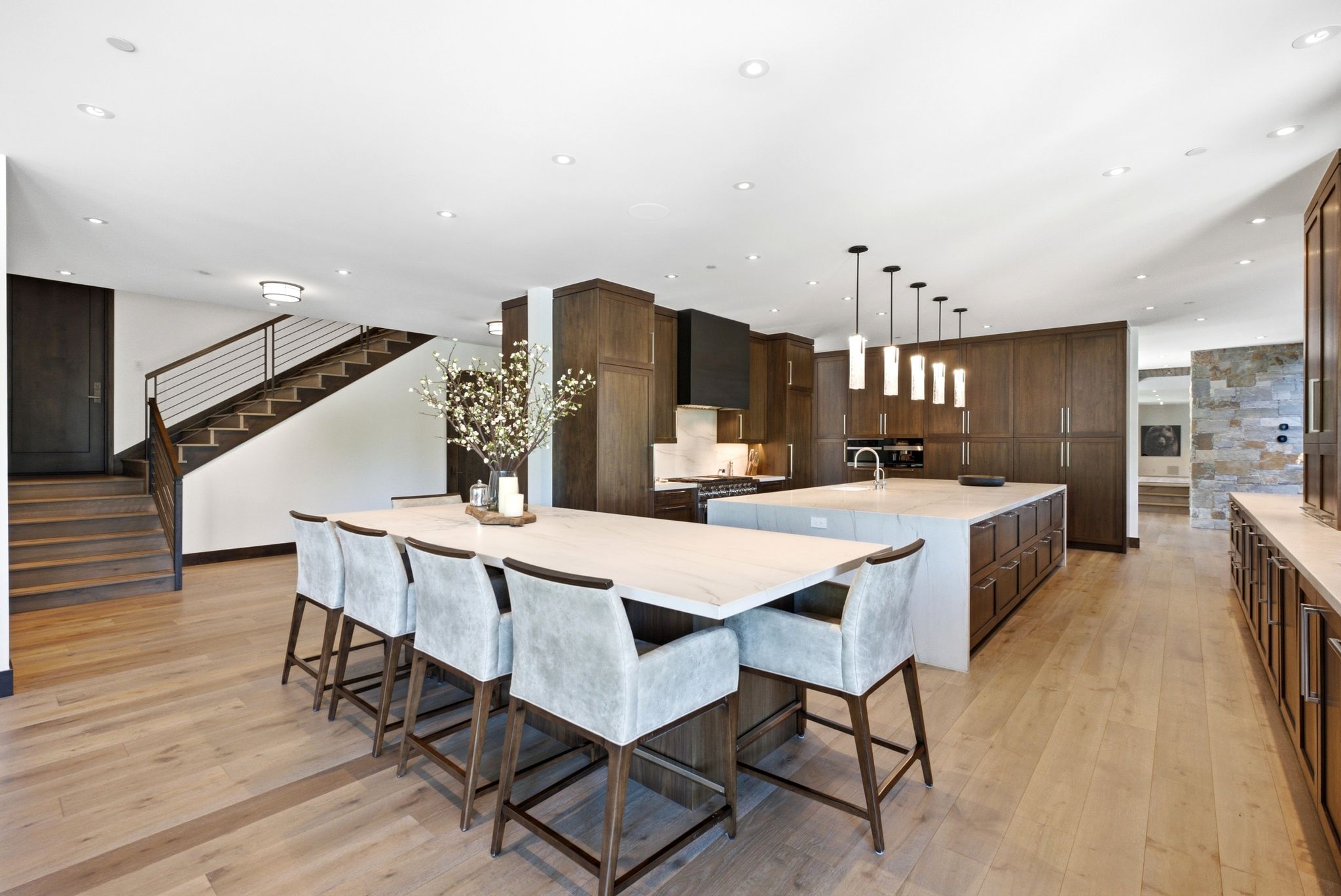 Expansive open-concept kitchen featuring two islands, light wood-finish flooring, dark wood cabinetry, and a black range hood