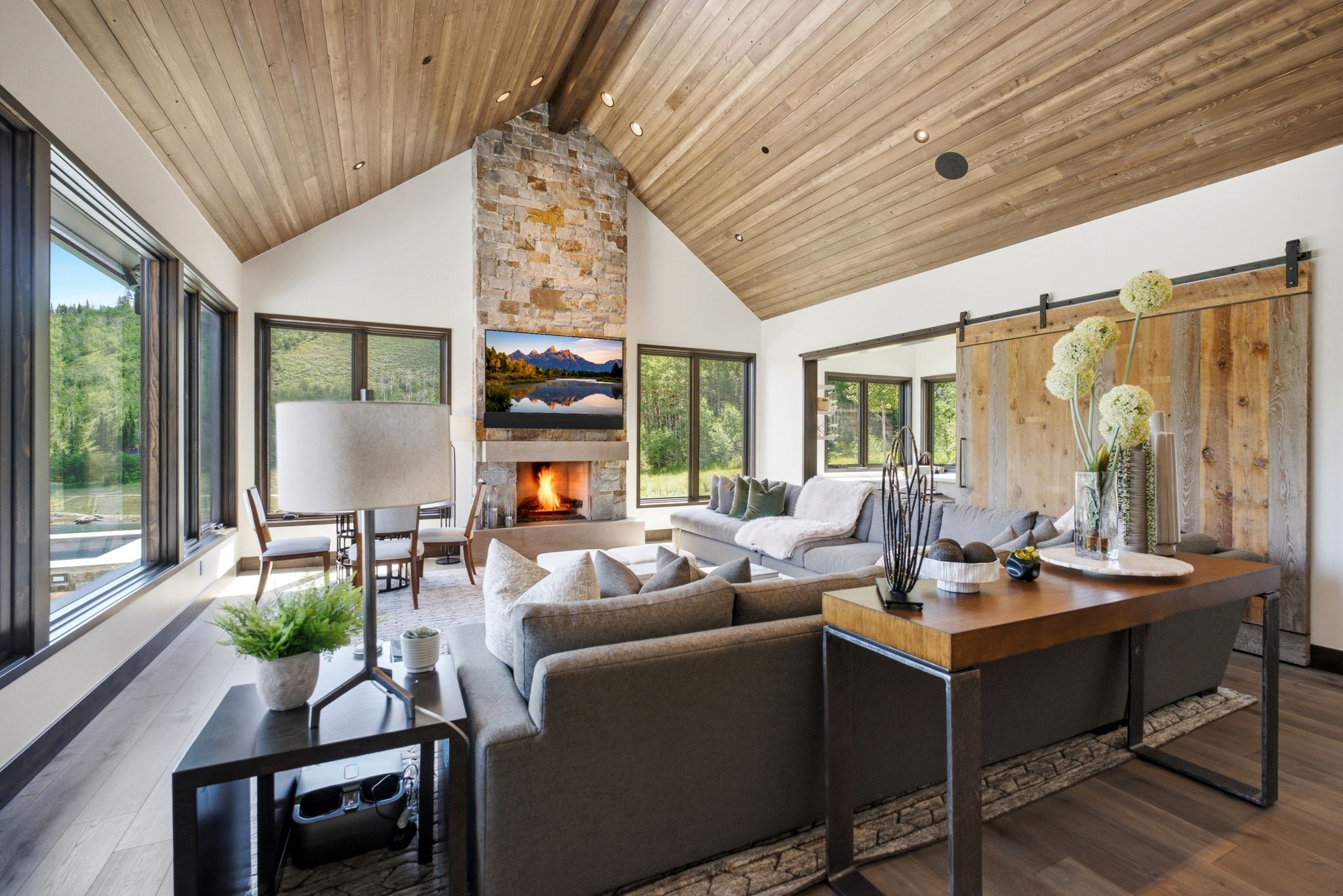 Great room featuring a vaulted wood-finish ceiling, a stone fireplace with a built-in hearth, and expansive windows
