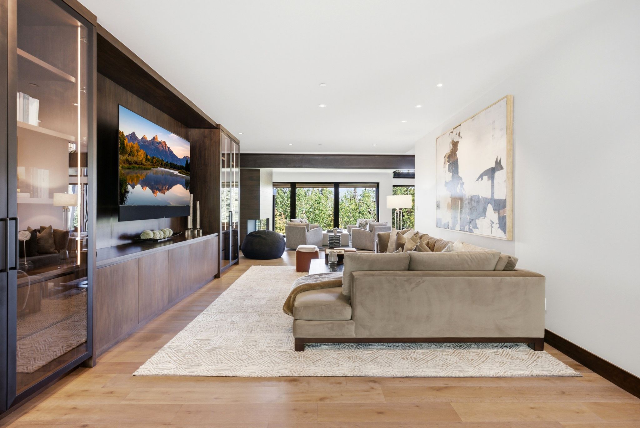 Open-concept living space featuring wood-finish flooring, a built-in media console with storage, floor-to-ceiling glass paneling, and recessed lighting throughout
