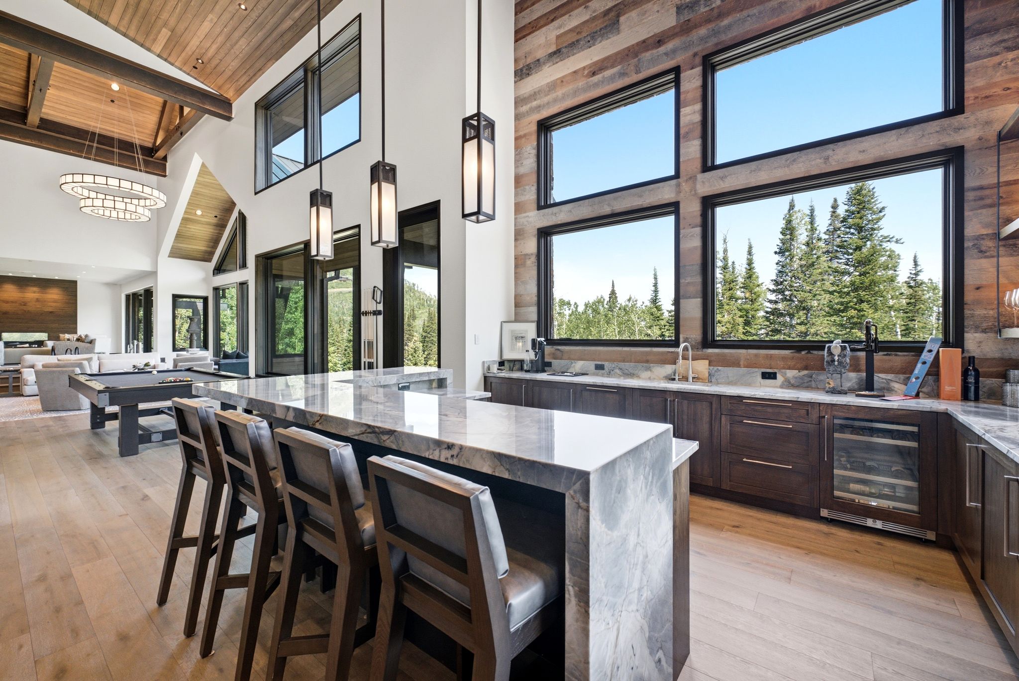 Spacious open-concept interior featuring light wood-finish flooring, a vaulted wood-paneled ceiling with exposed beams, and a large kitchen island with stone countertop