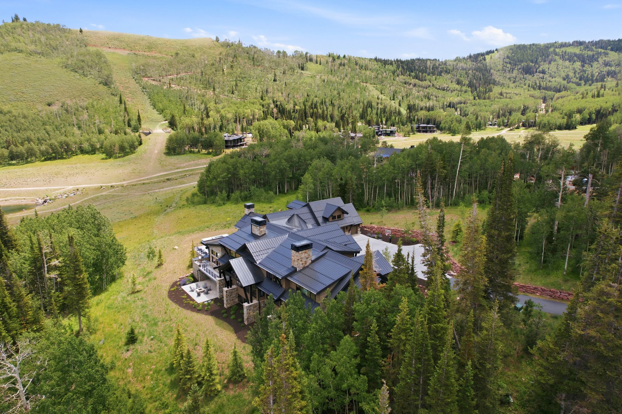 Expansive mountain estate featuring a multi-level structure with stone and wood siding, a dark metal roof, and multiple chimneys
