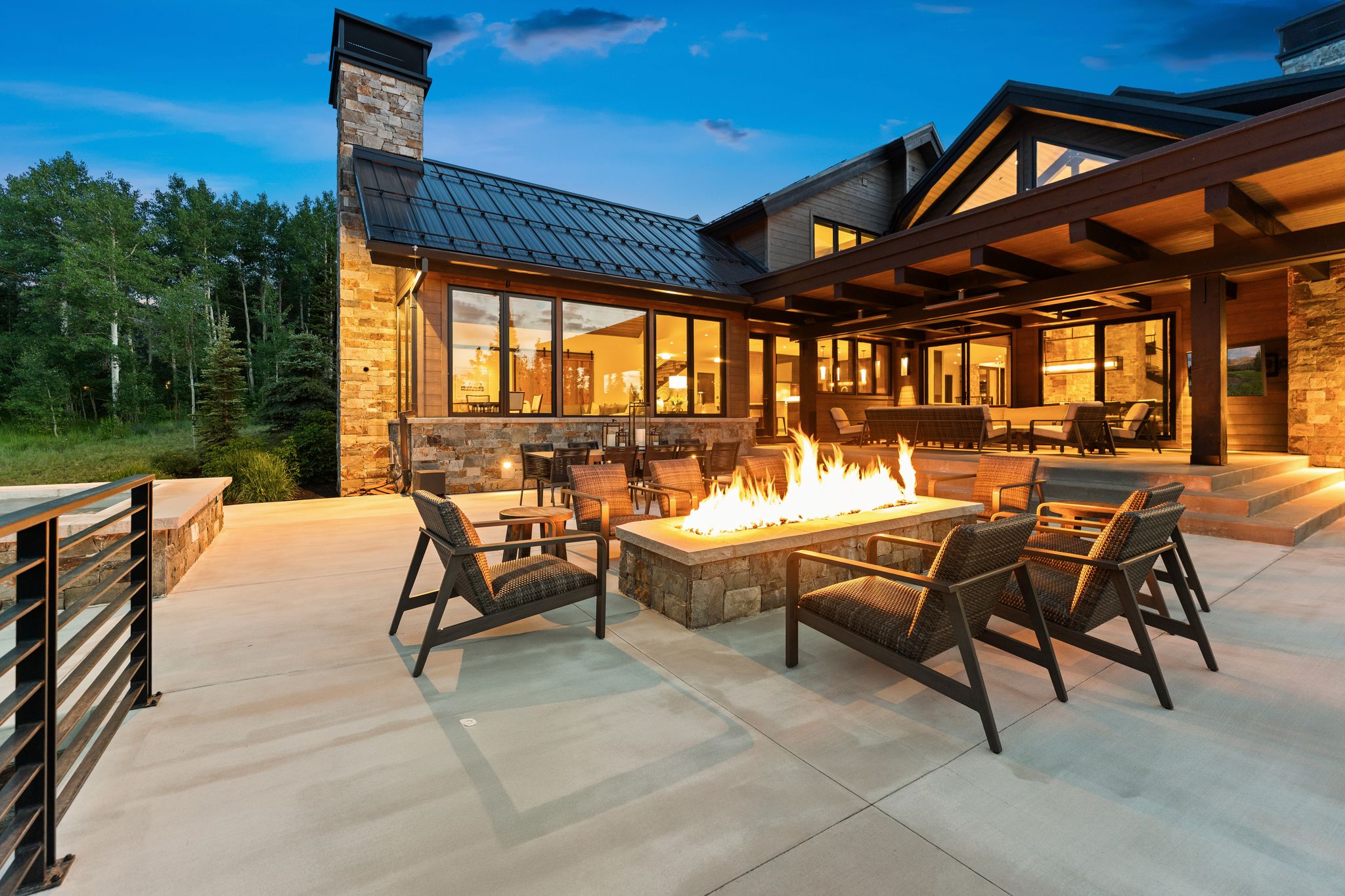Expansive outdoor patio featuring a stone fire pit, extensive concrete hardscaping, and a metal railing system