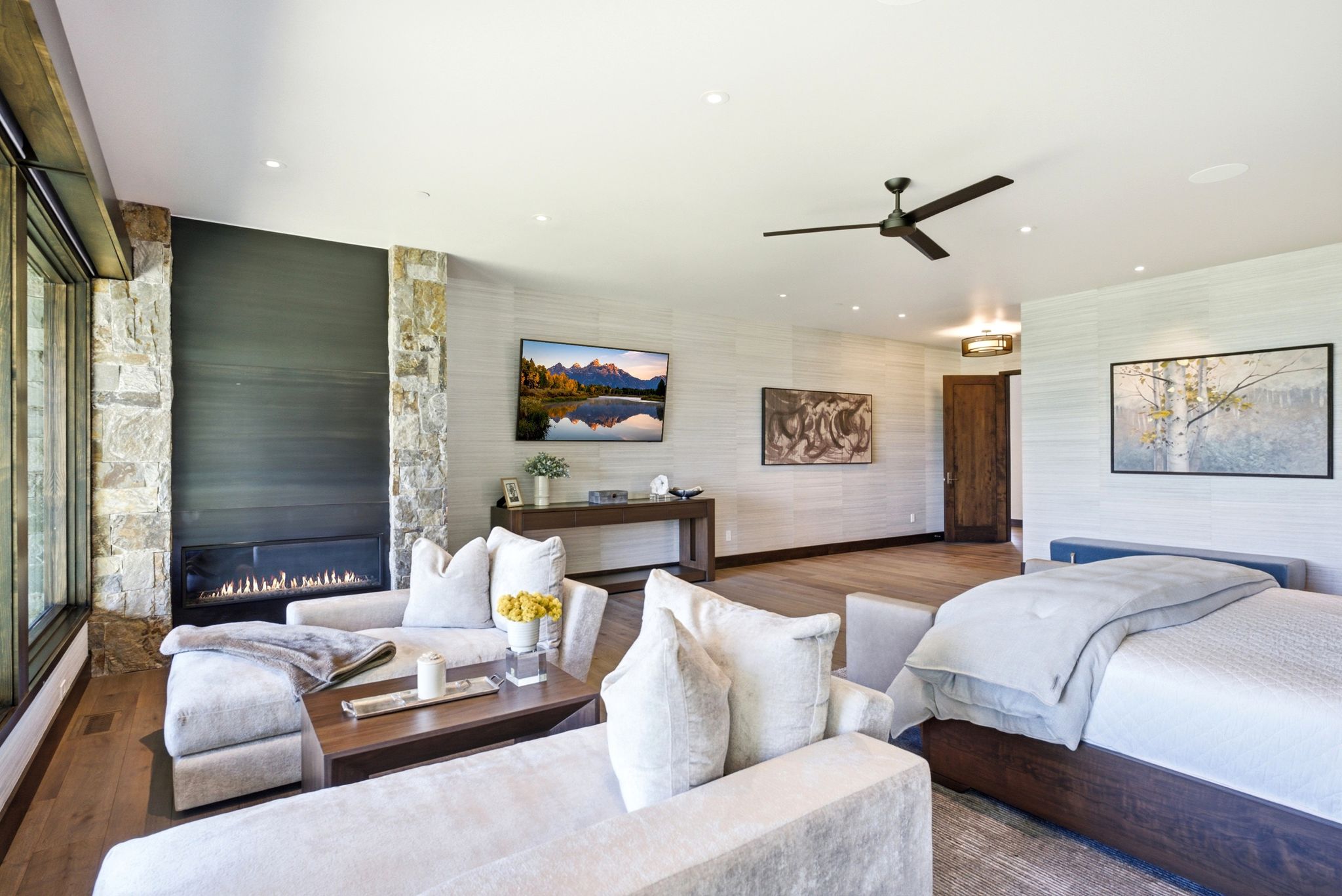 Expansive interior space featuring wood-finish flooring, a linear fireplace set in stone, and large windows