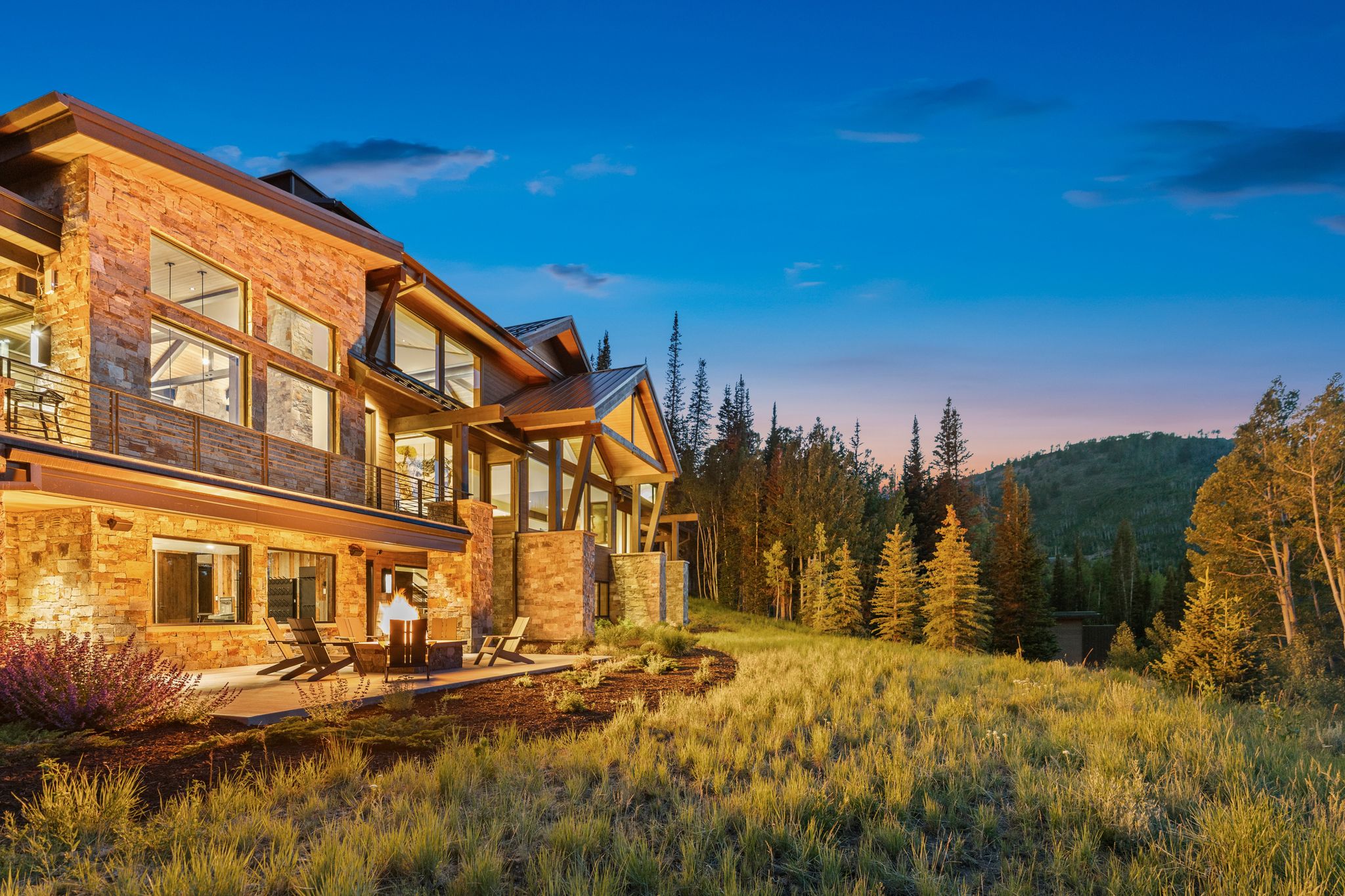 Stone and timber framed exterior featuring multiple window banks, a covered patio with a built-in fire feature, and a second-story balcony