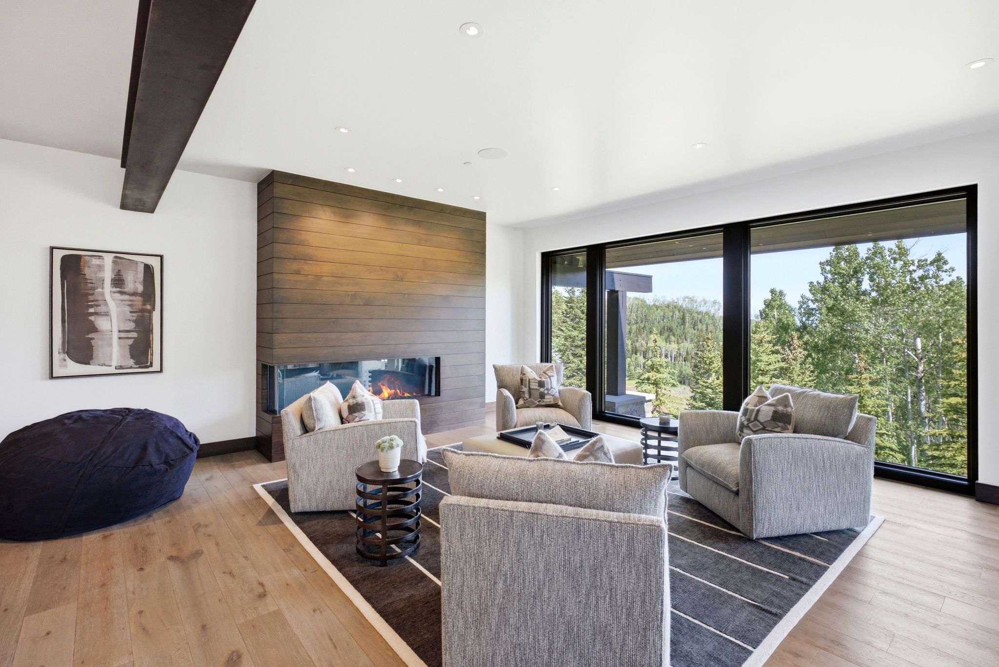 Spacious living area featuring expansive floor-to-ceiling windows, a wood-paneled fireplace, recessed lighting, and wood-finish flooring