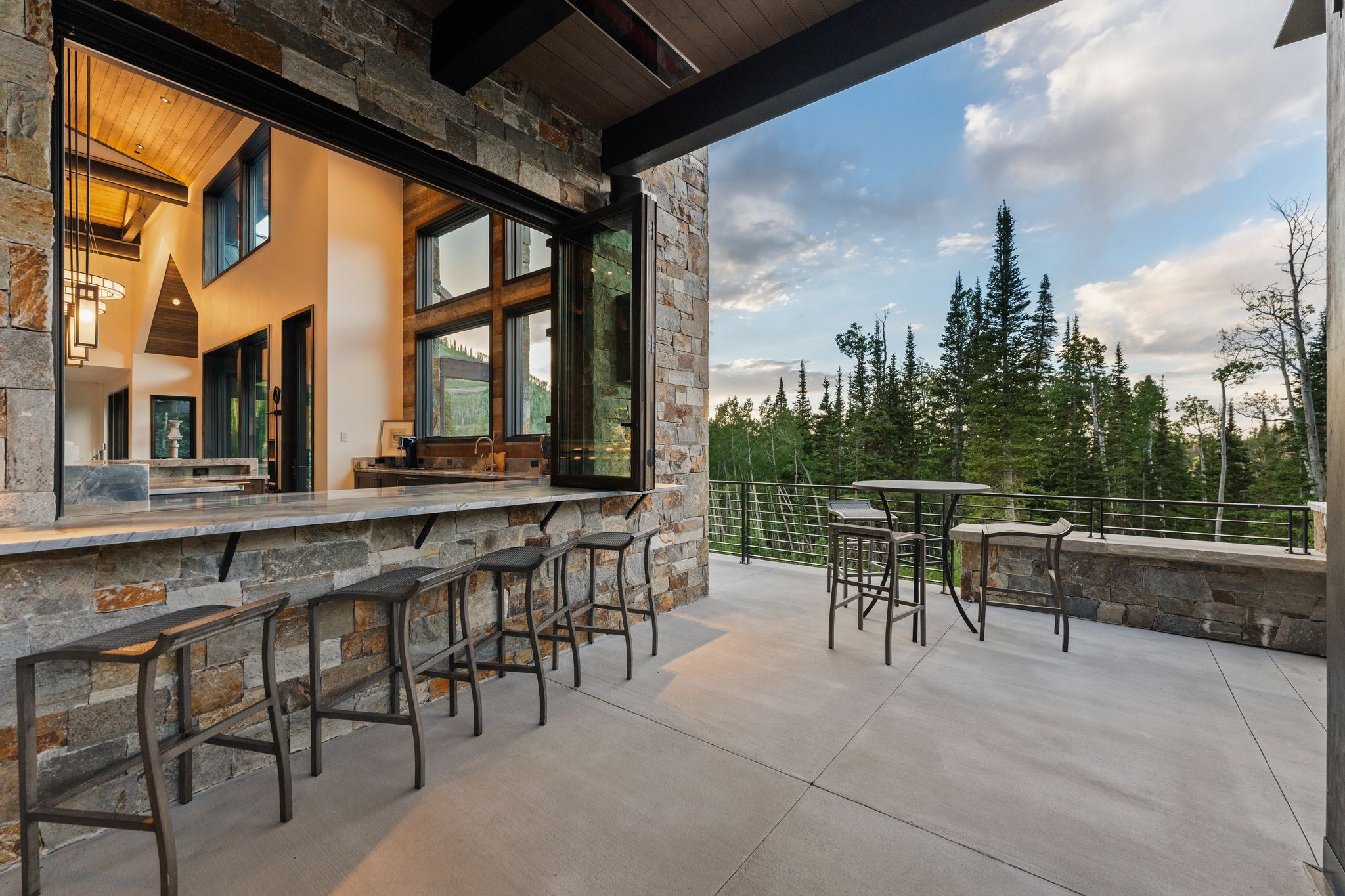 Expansive stone patio featuring a built-in outdoor bar with seating and a folding window system