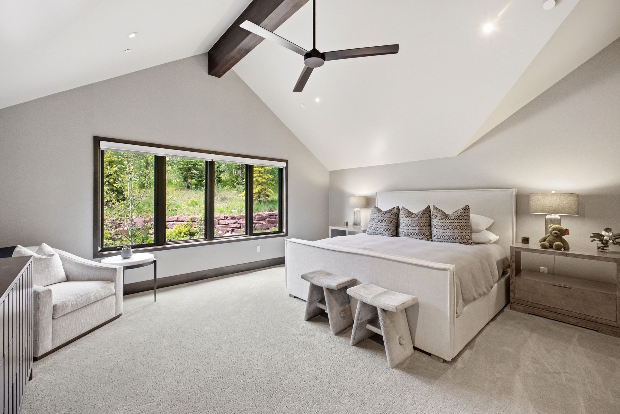 Spacious room featuring vaulted ceilings with exposed wood beams, a modern ceiling fan, large windows with dark trim, recessed lighting, and light-toned carpeting