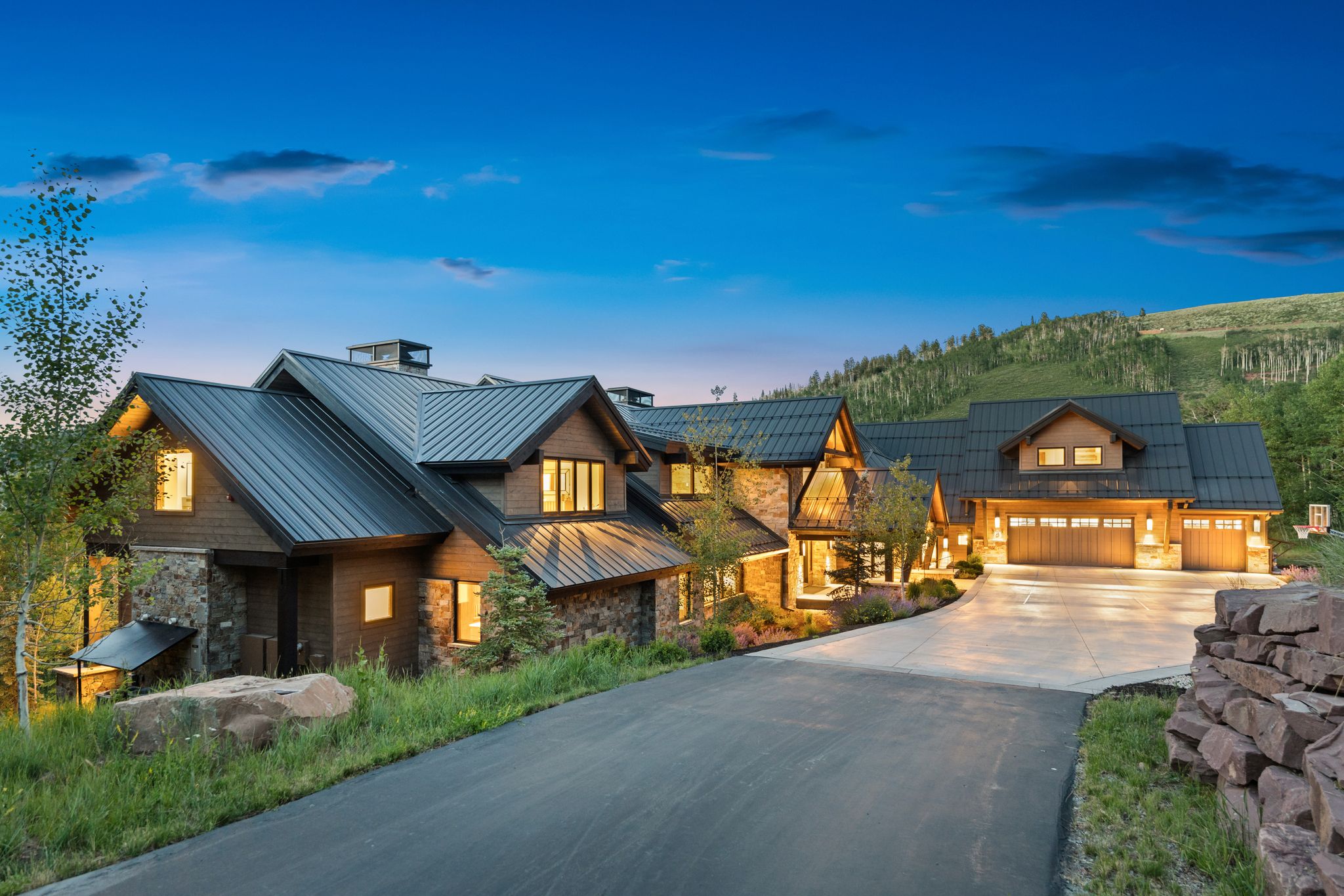 Multi-level mountain-style residence featuring a metal roof, stone and wood-finish siding, and multiple attached garages