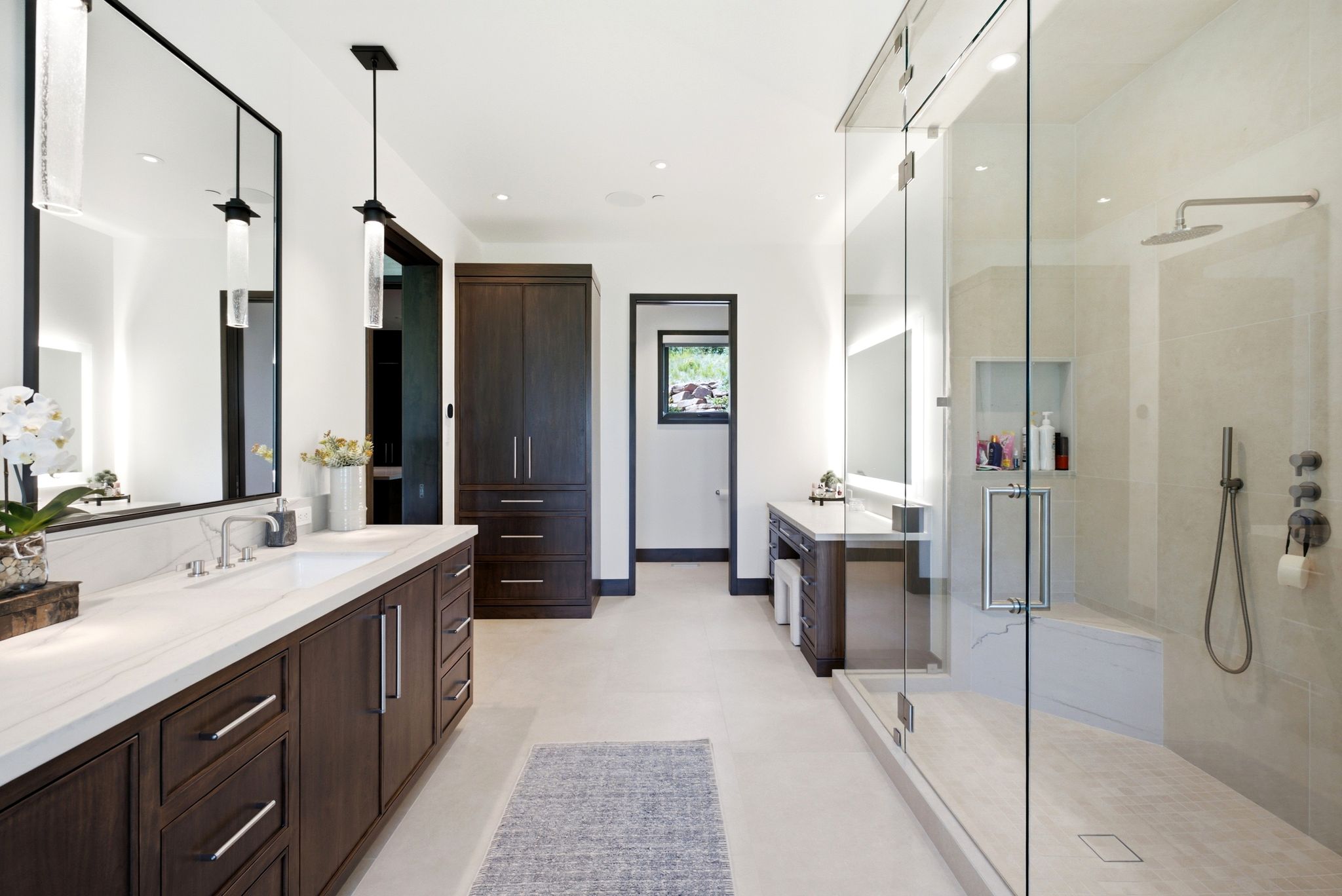 Spacious bathroom featuring a frameless glass shower enclosure with a built-in bench, dual vanity with a white countertop, dark wood-finish cabinetry, and recessed lighting