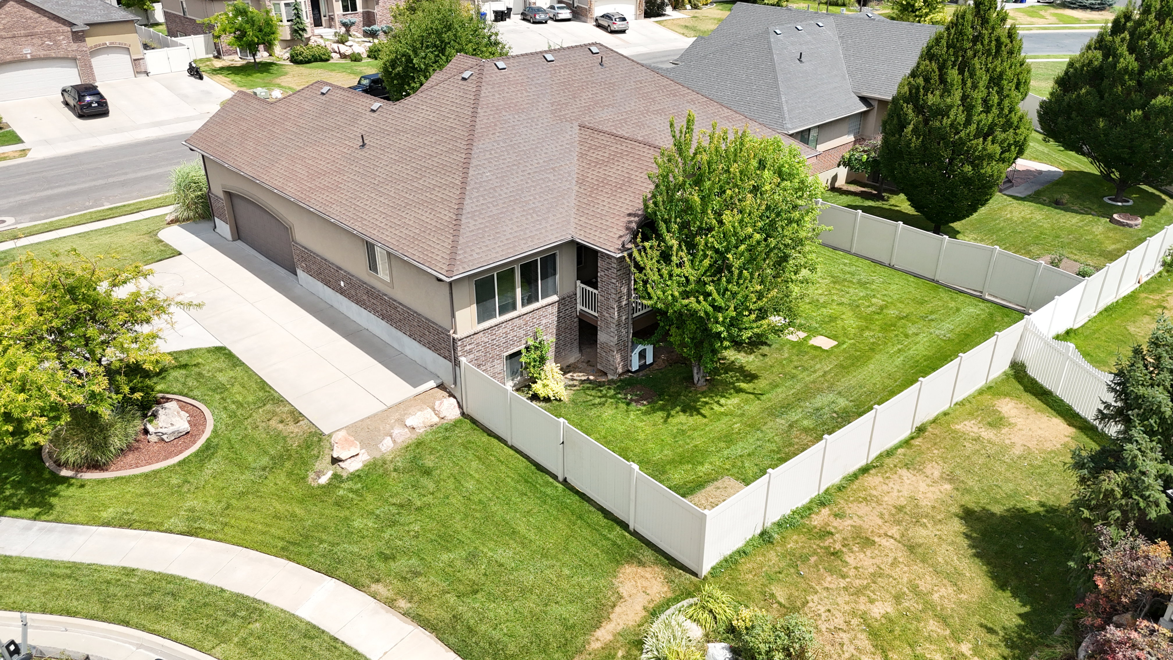 Two-story exterior with brick and siding facade, featuring a private fenced yard, mature trees, an attached garage, and a concrete driveway