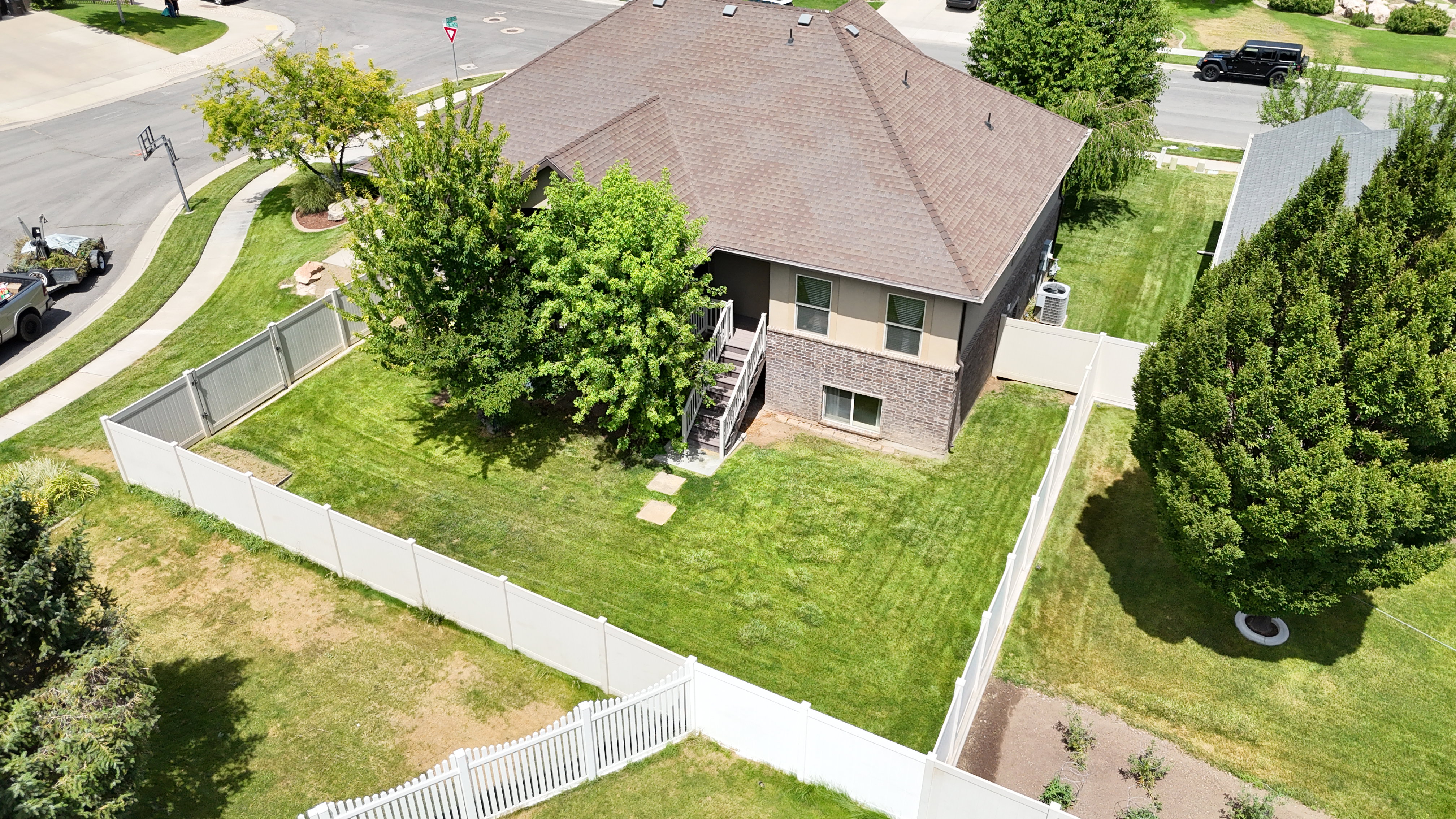 Expansive backyard featuring a manicured lawn, full privacy fencing, established trees, and a concrete patio