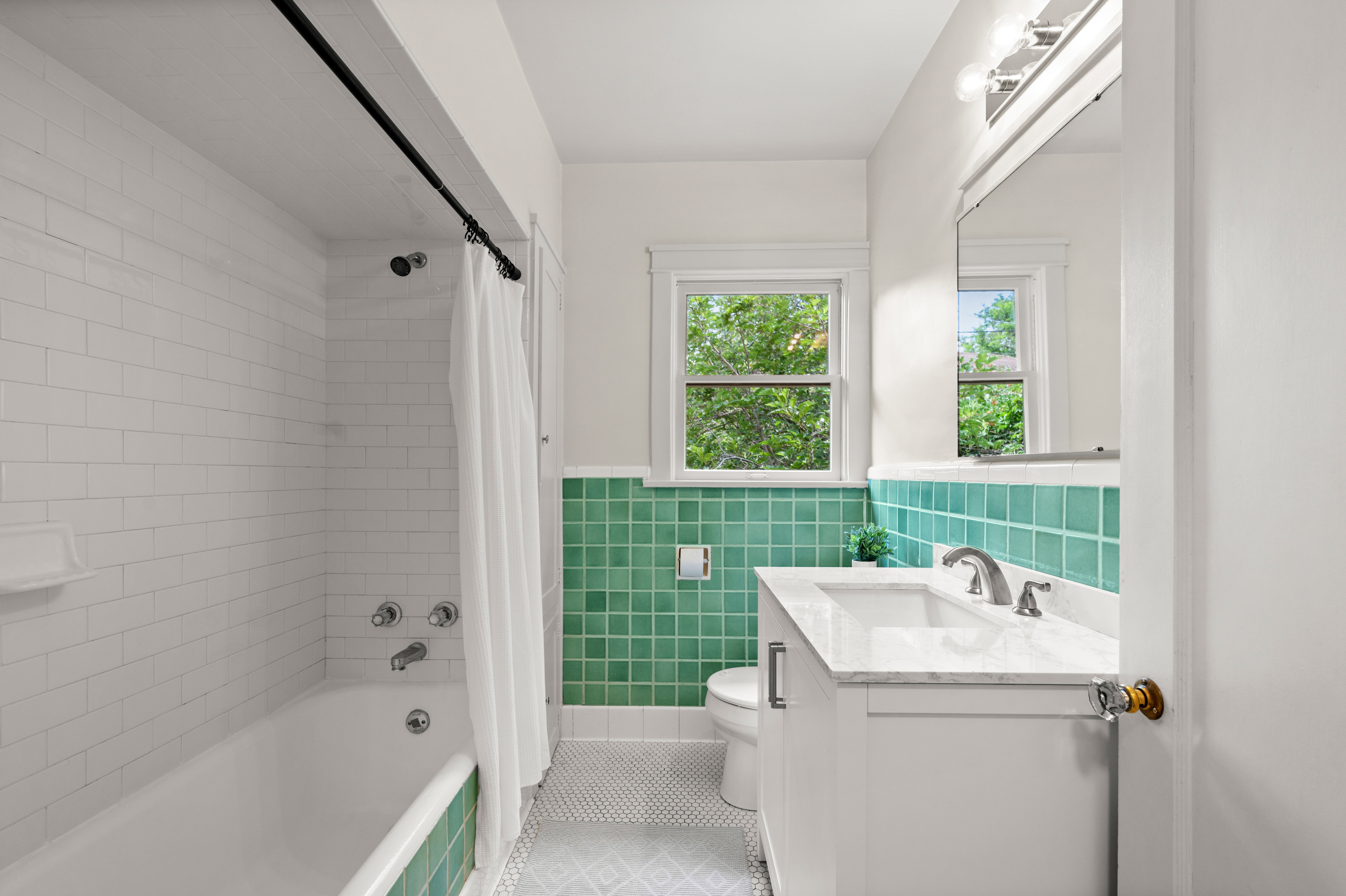 Bathroom featuring a single vanity with a white countertop and undermount sink, a white bathtub with subway tile surround, green square wall tiles, and a window