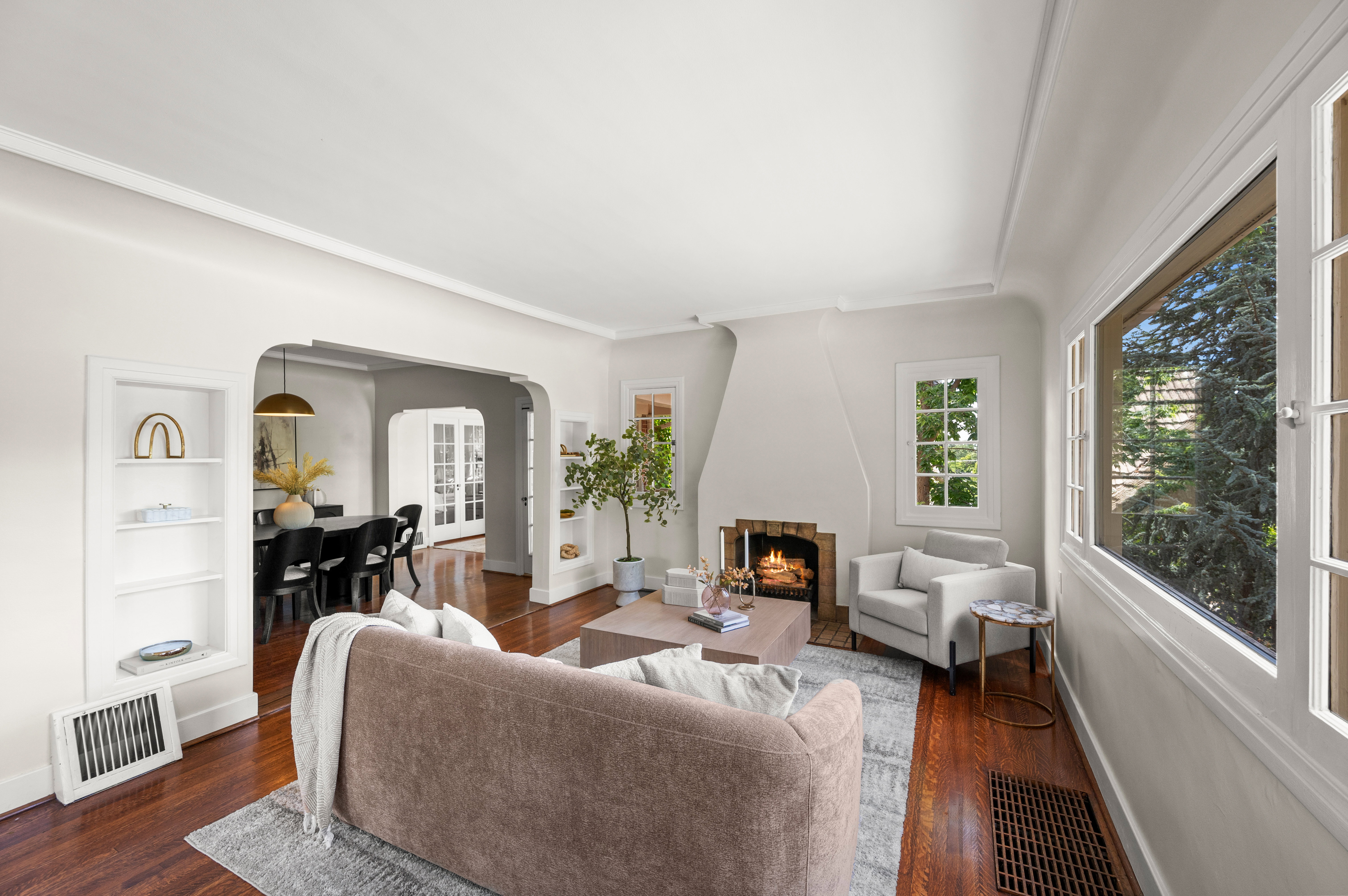 Hardwood flooring throughout the living area, featuring a fireplace with brick surround, built-in shelving, and large windows