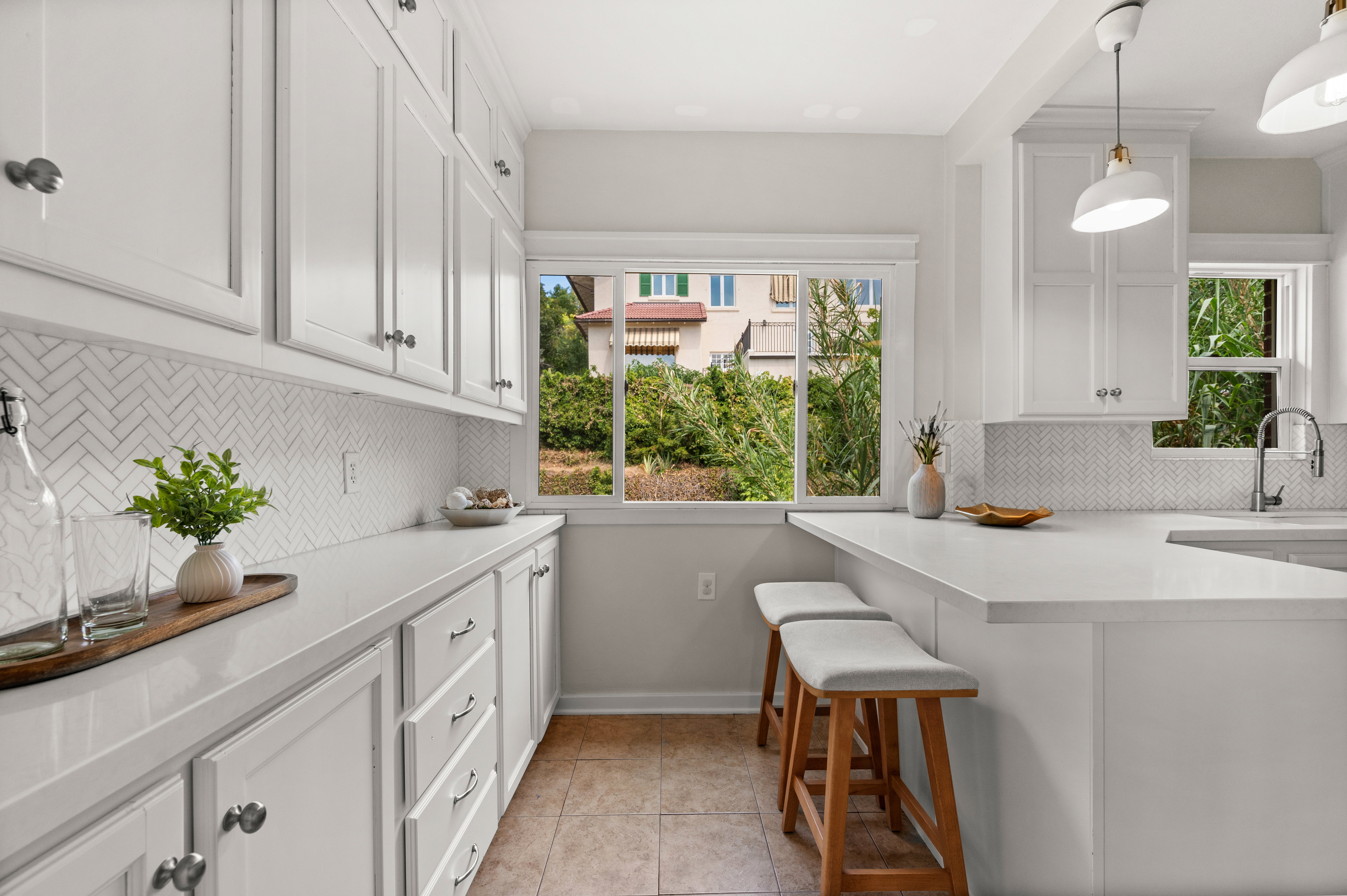Kitchen featuring white shaker-style cabinetry, a white herringbone tile backsplash, and light-toned countertops