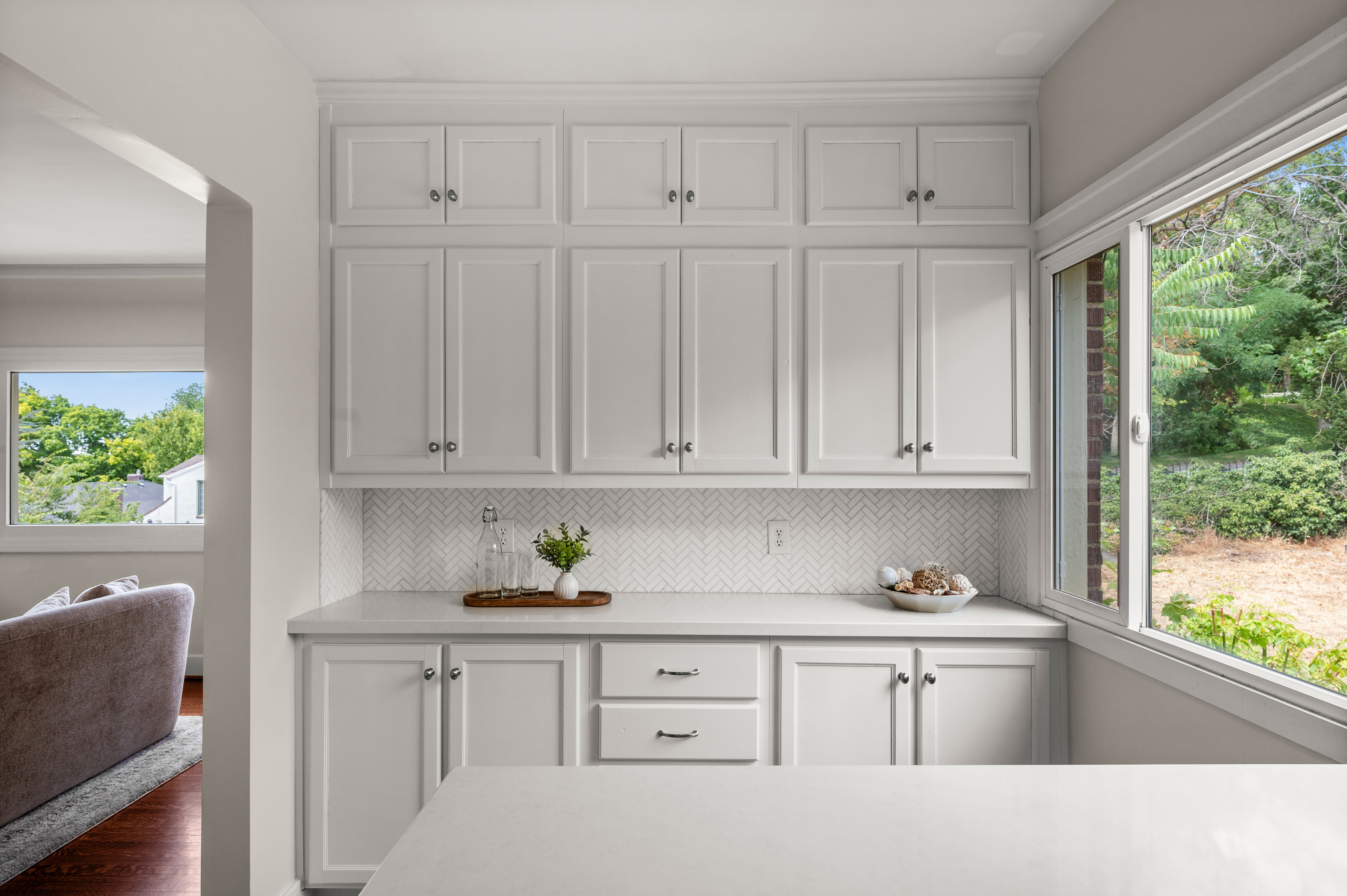 Extensive white cabinetry with crown molding, light-toned countertops, and a white herringbone tile backsplash