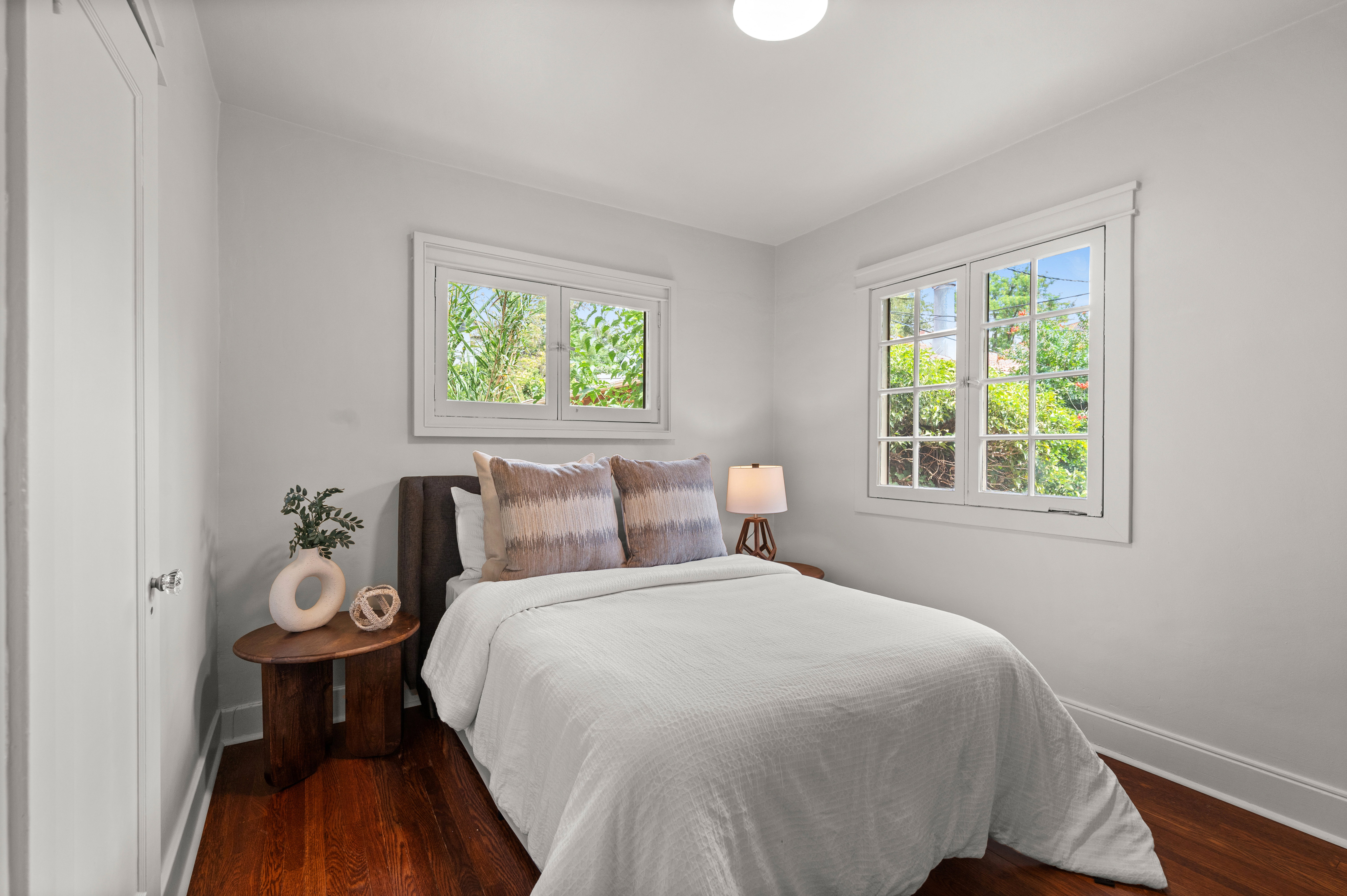 Light-filled room featuring two multi-pane windows, wood-finish flooring, white baseboards, and crown molding