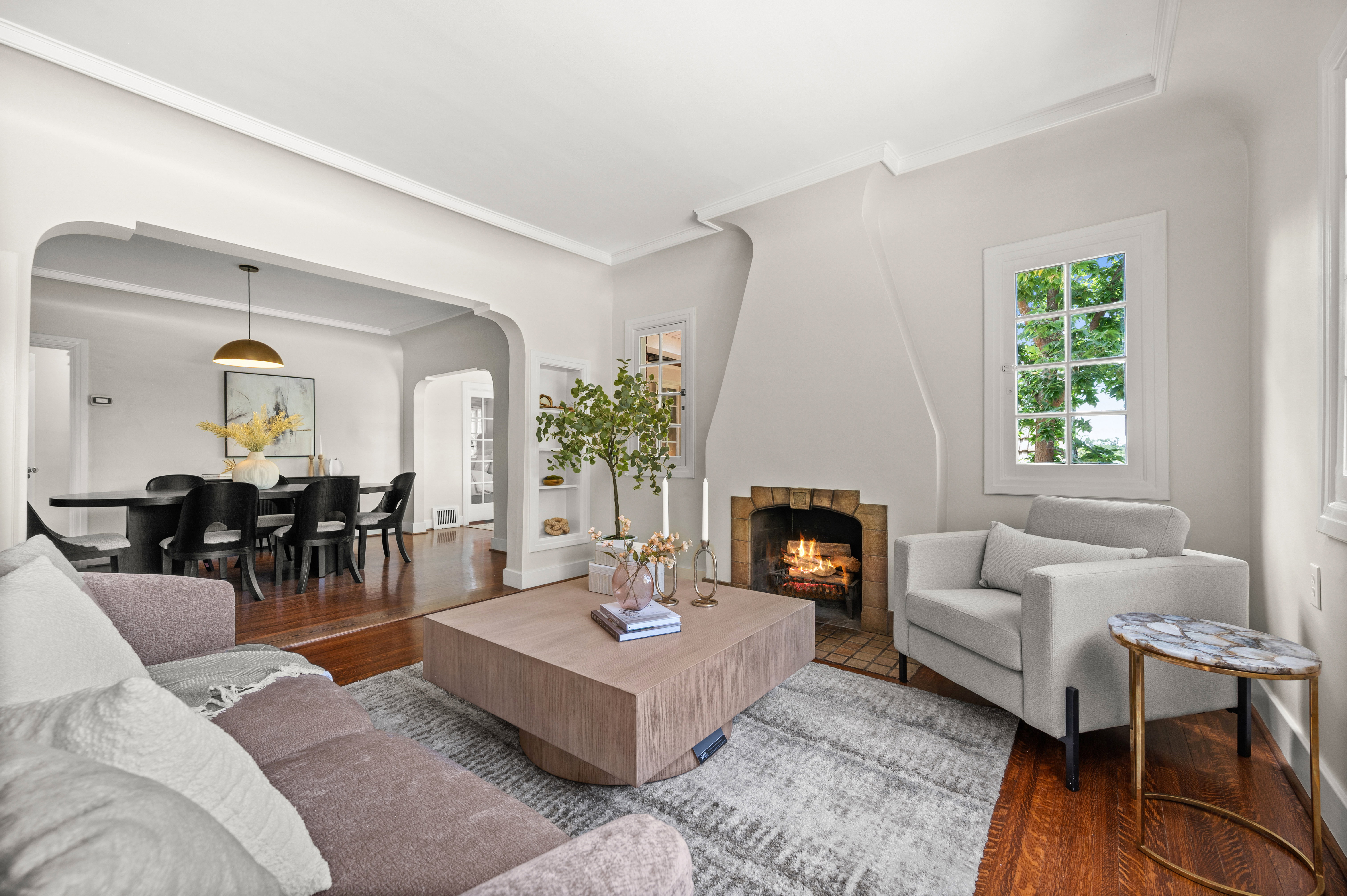 Living room featuring a prominent fireplace with a brick surround, hardwood flooring, and a large window with multiple panes