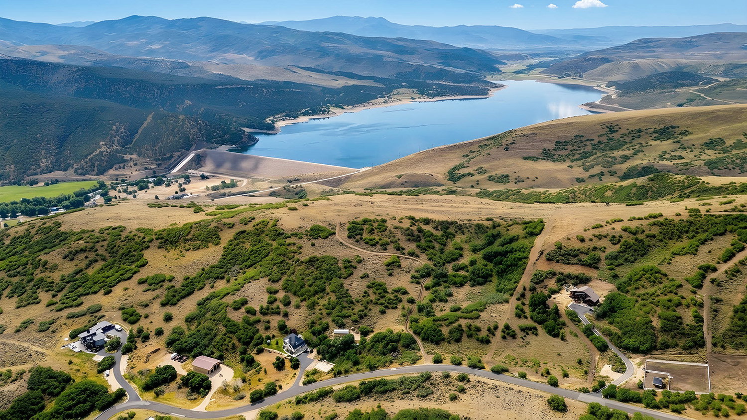 Expansive hillside property with a distant lake, surrounded by mountains and sparse vegetation