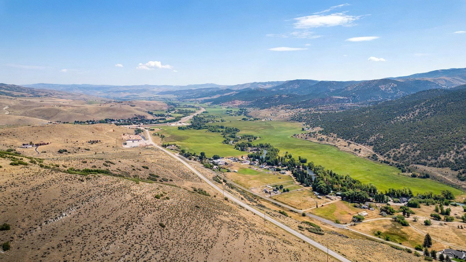 Expansive aerial showcasing a broad valley with a verdant river corridor flanked by arid hillsides