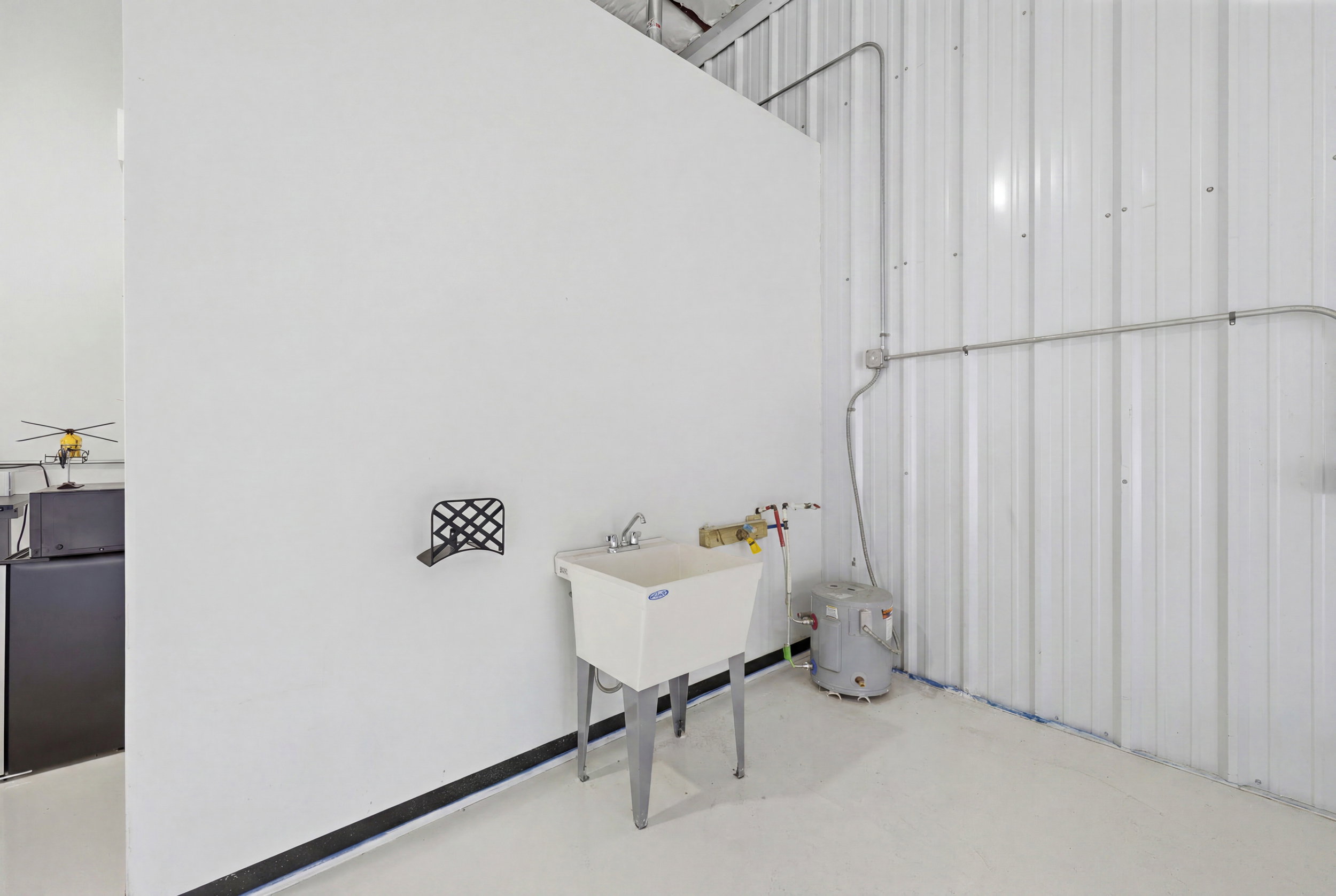 Utility sink area featuring a white basin, exposed plumbing, and a compact water heater