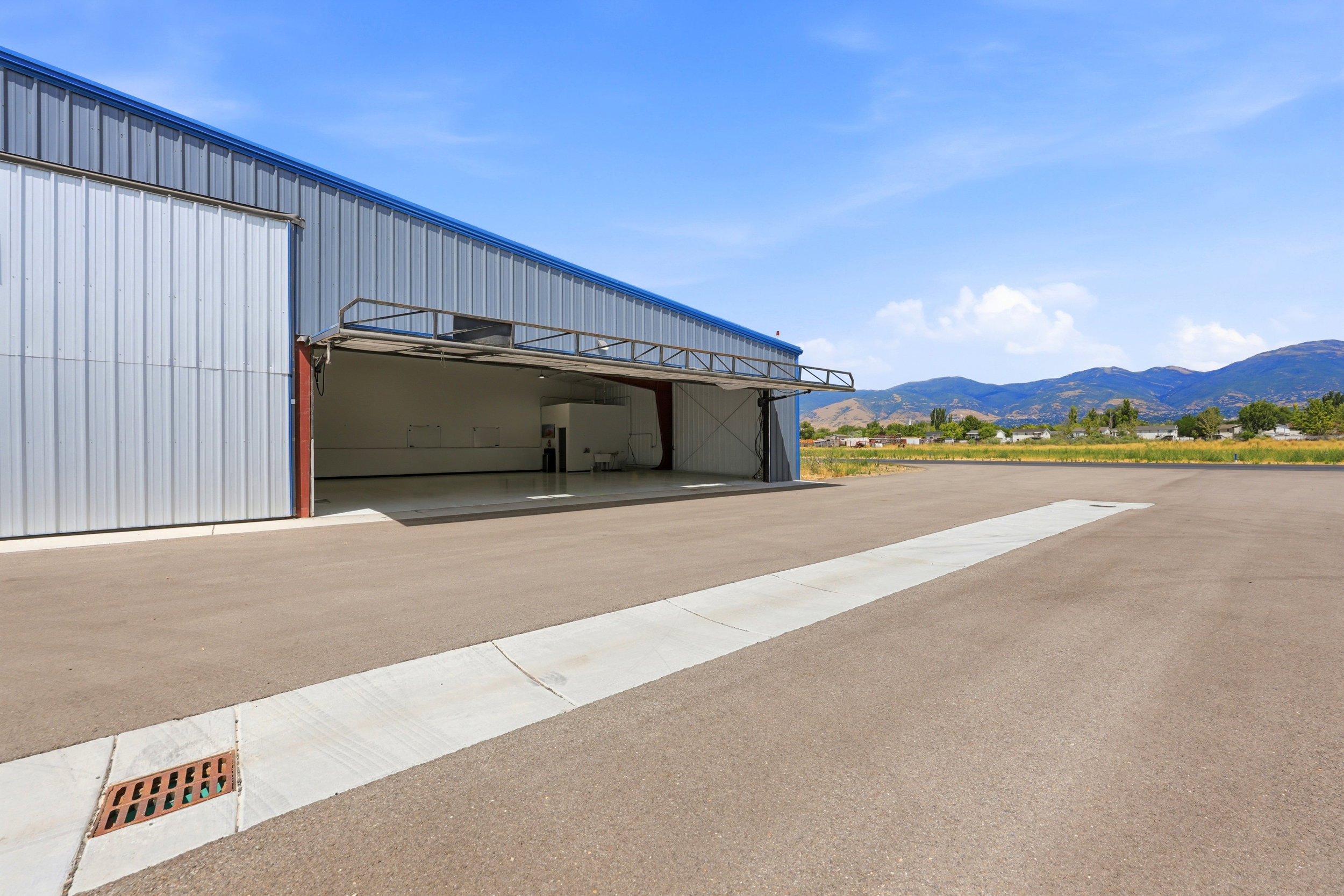 Large metal-sided commercial building featuring a bi-fold hangar door and an expansive asphalt apron