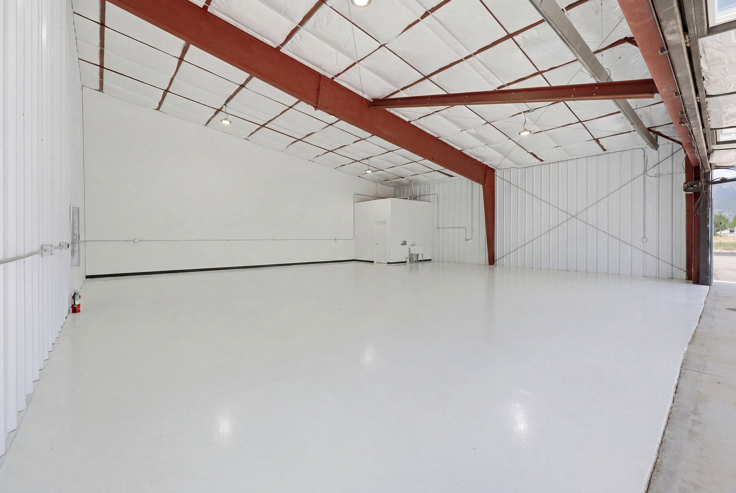 Spacious open-concept warehouse featuring high ceilings with exposed structural beams, white walls, and a light-colored finished concrete floor