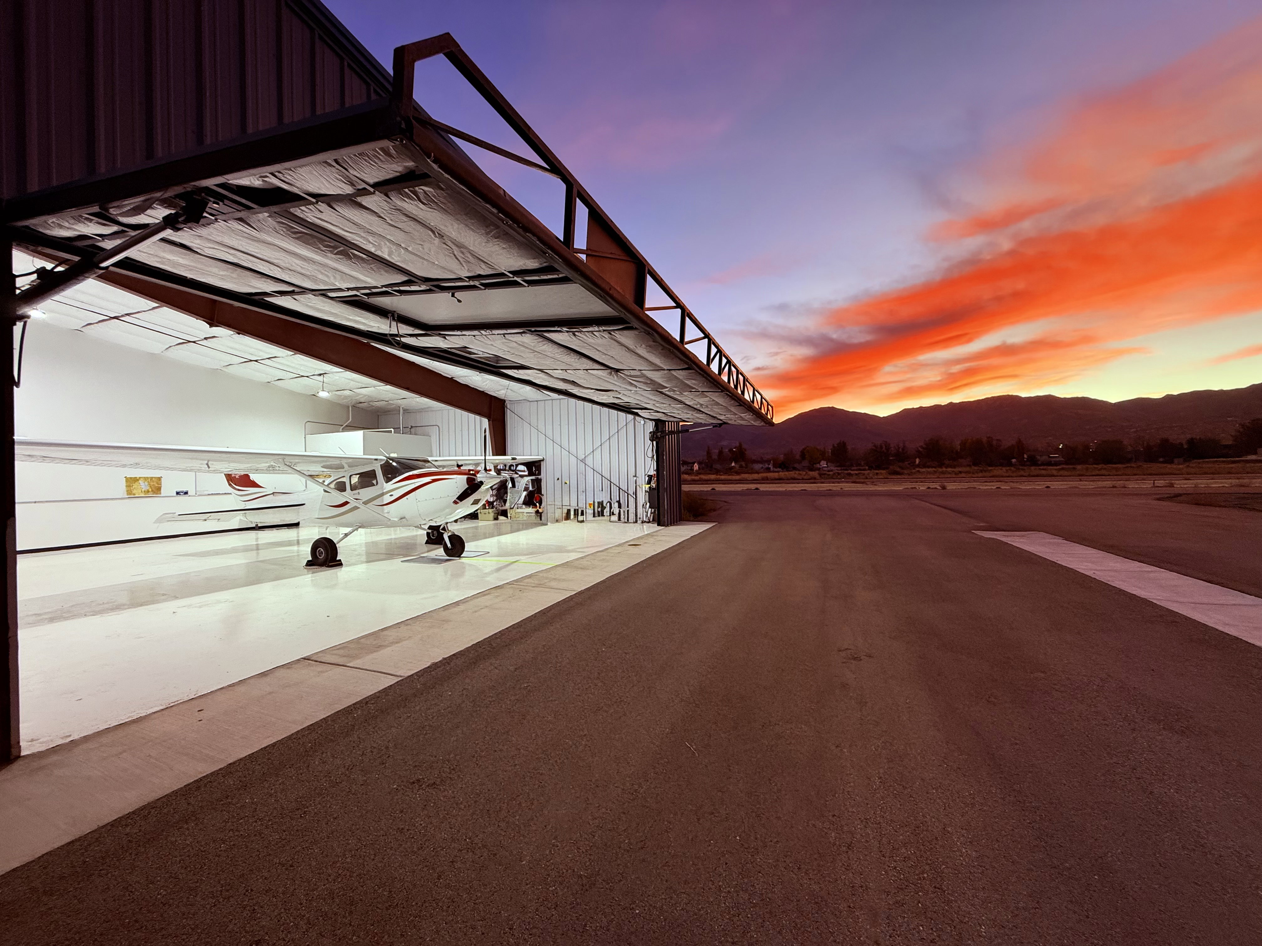 Aircraft hangar featuring a bi-fold door, corrugated metal exterior, and a paved runway apron