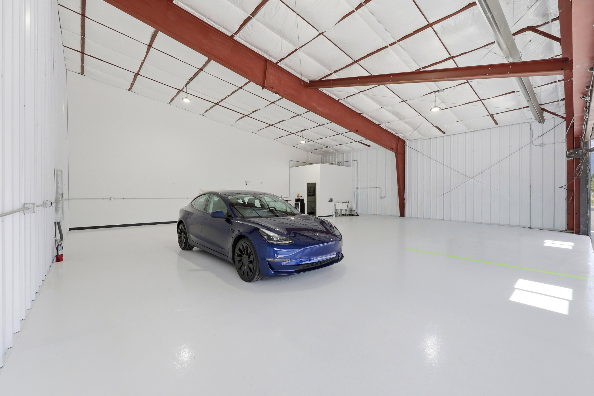 Expansive warehouse space featuring a high-gloss concrete floor, exposed red steel beam construction, insulated ceiling, and corrugated metal wall panels