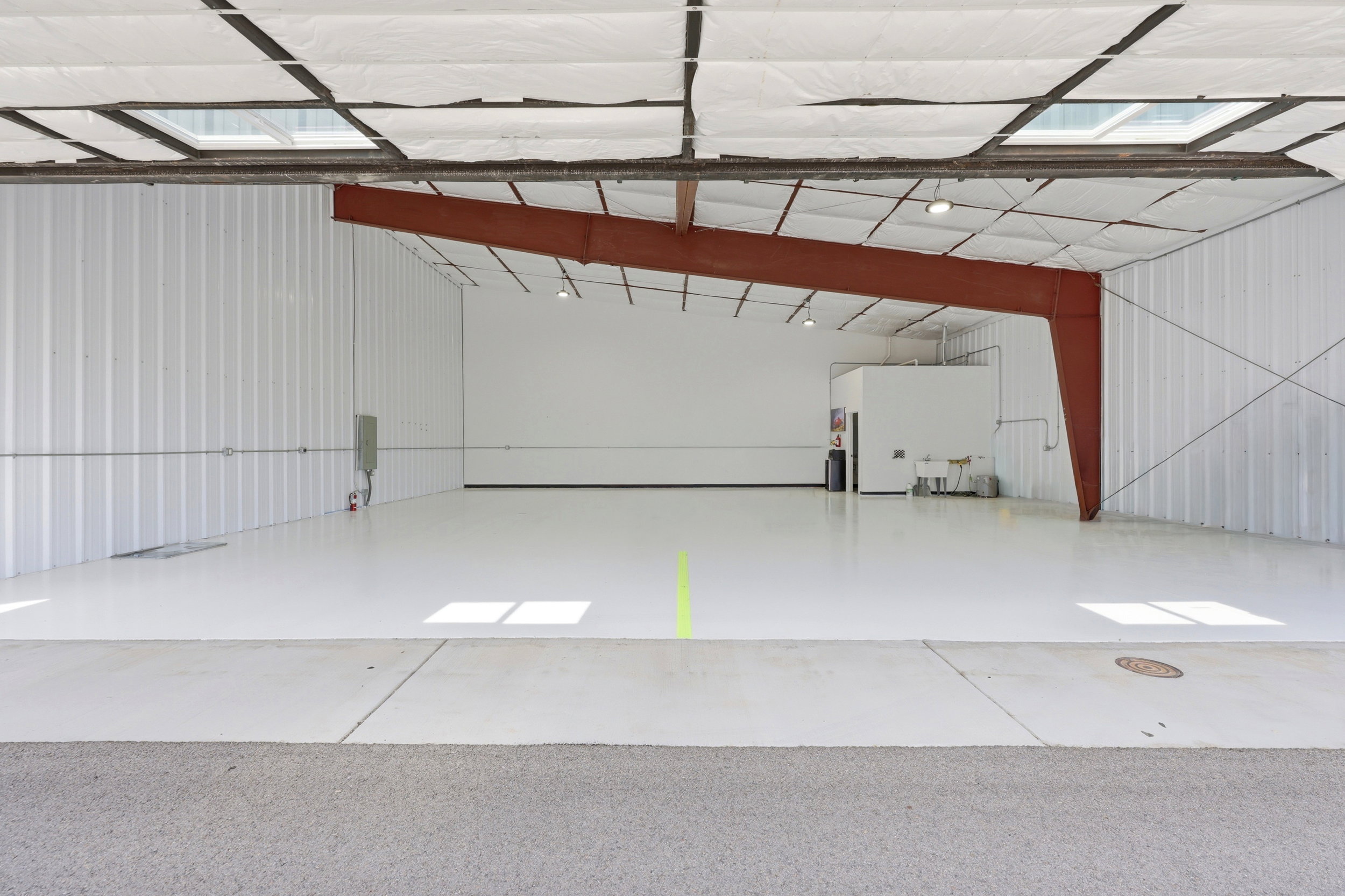 Spacious commercial interior featuring a polished concrete floor, corrugated metal walls, exposed structural beams, and skylights providing natural illumination