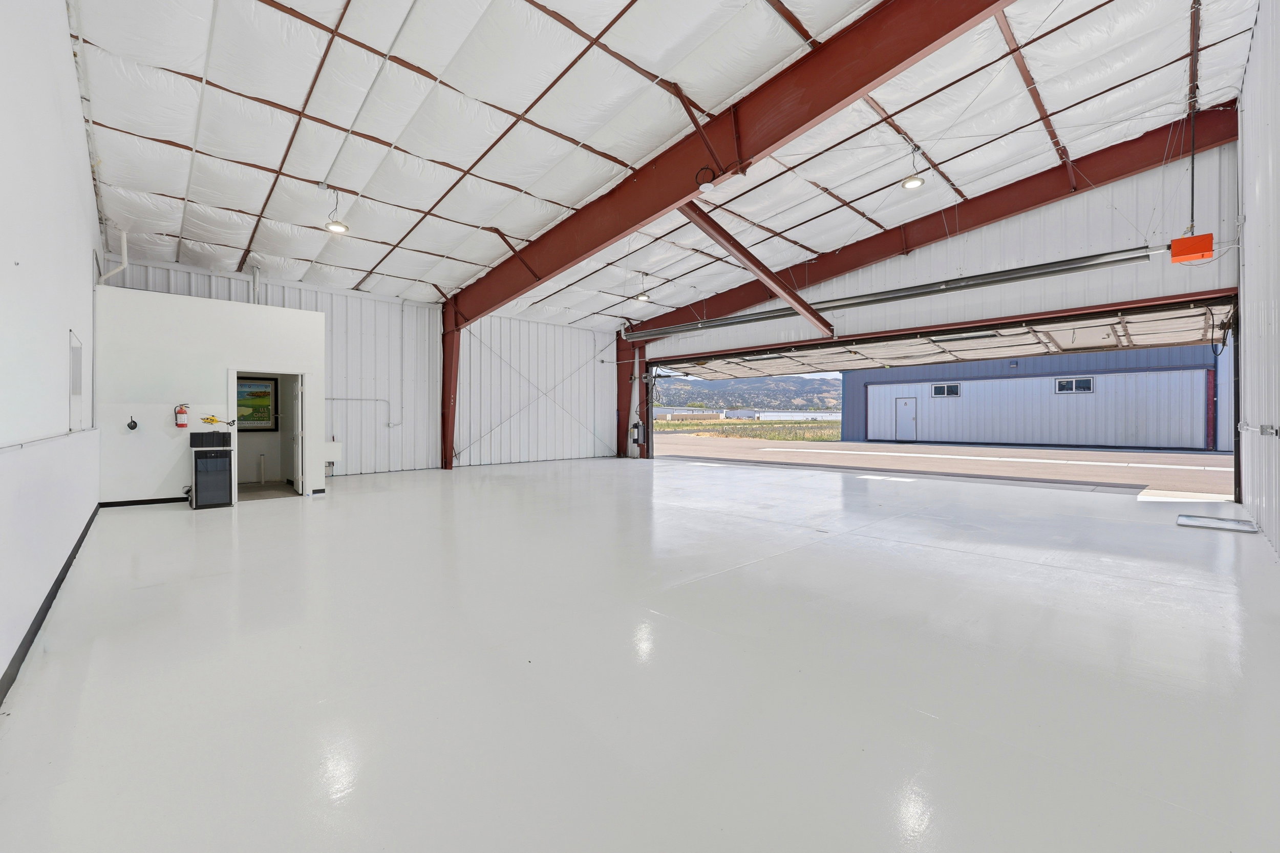 Spacious industrial interior featuring polished concrete flooring, exposed red steel structural beams, and a high insulated ceiling