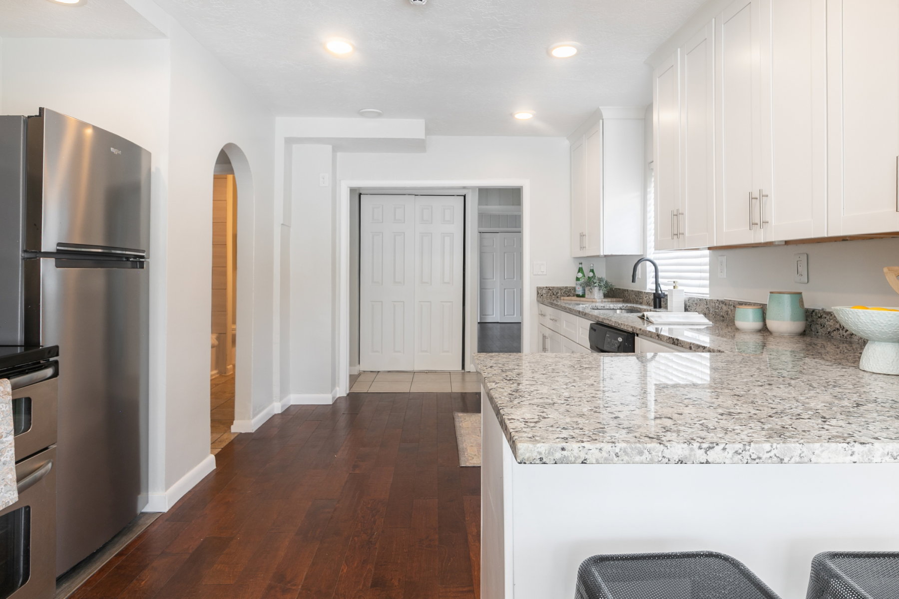 Contemporary kitchen featuring a breakfast bar with stone-finish countertops, white cabinetry, stainless steel appliances, and wood-finish flooring