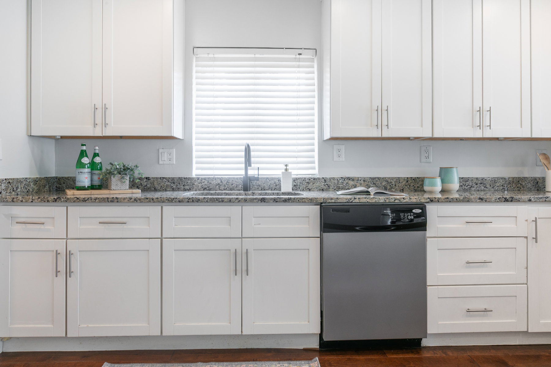 White shaker cabinetry with brushed nickel hardware, speckled countertops, stainless steel dishwasher, undermount sink, and wood-finish flooring