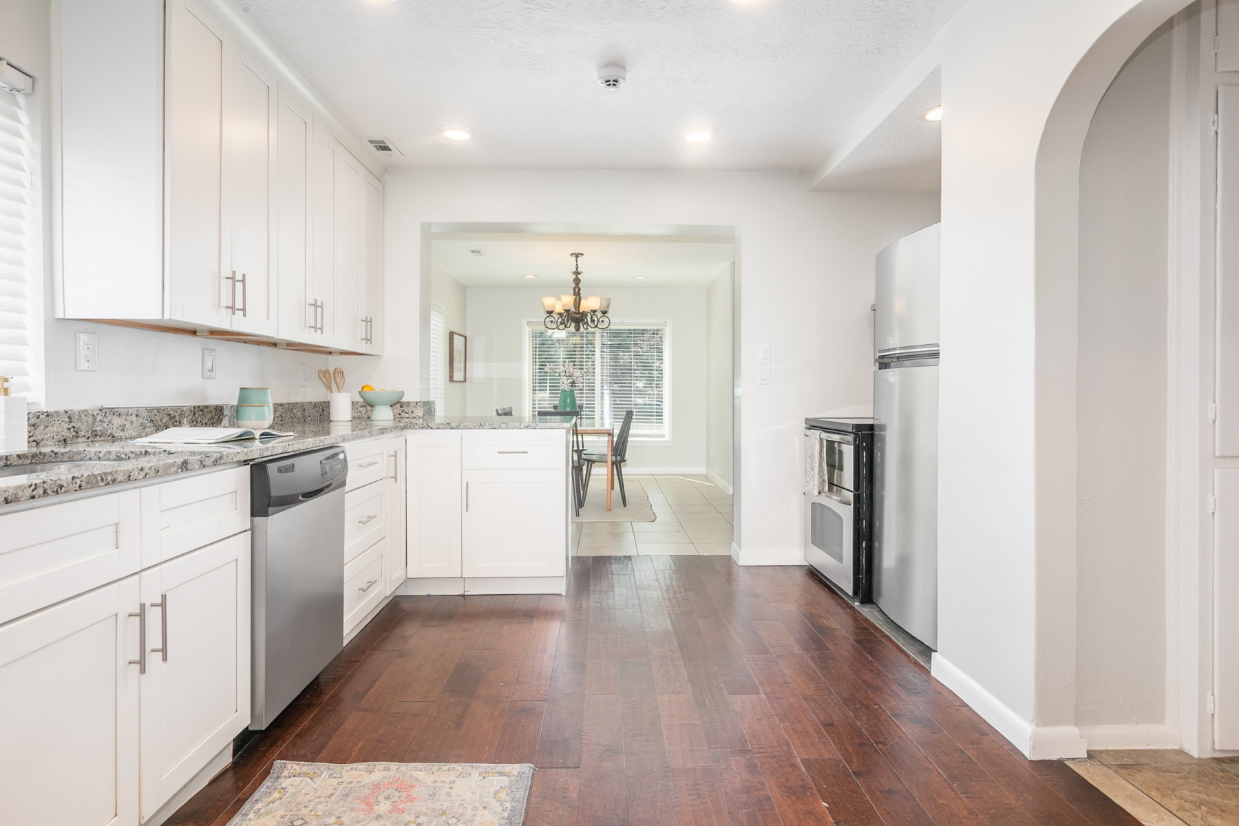 Kitchen featuring white shaker cabinetry, stainless steel appliances, speckled stone countertops, and wood-finish flooring