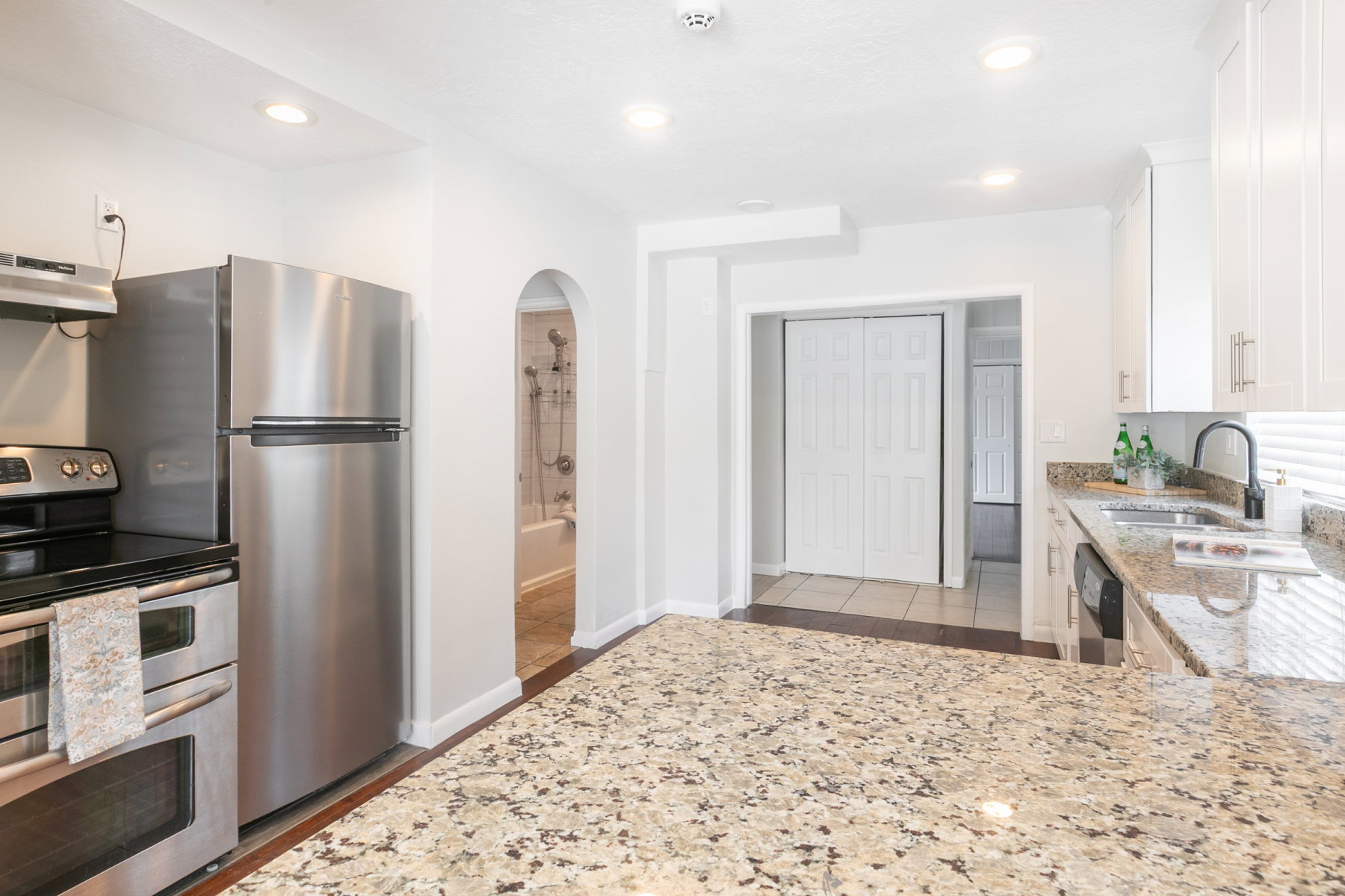Kitchen featuring a large speckled countertop, stainless steel appliances, white cabinetry with silver hardware, and recessed lighting