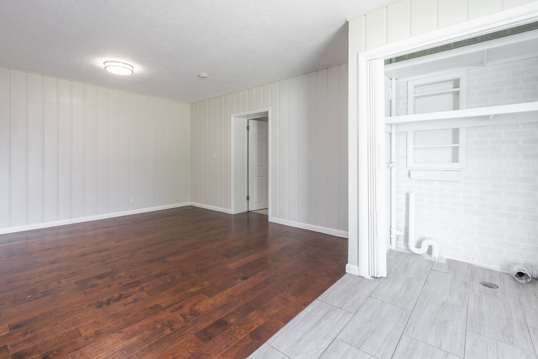 Spacious room featuring rich wood-finish flooring, vertical paneling, and a flush mount ceiling light