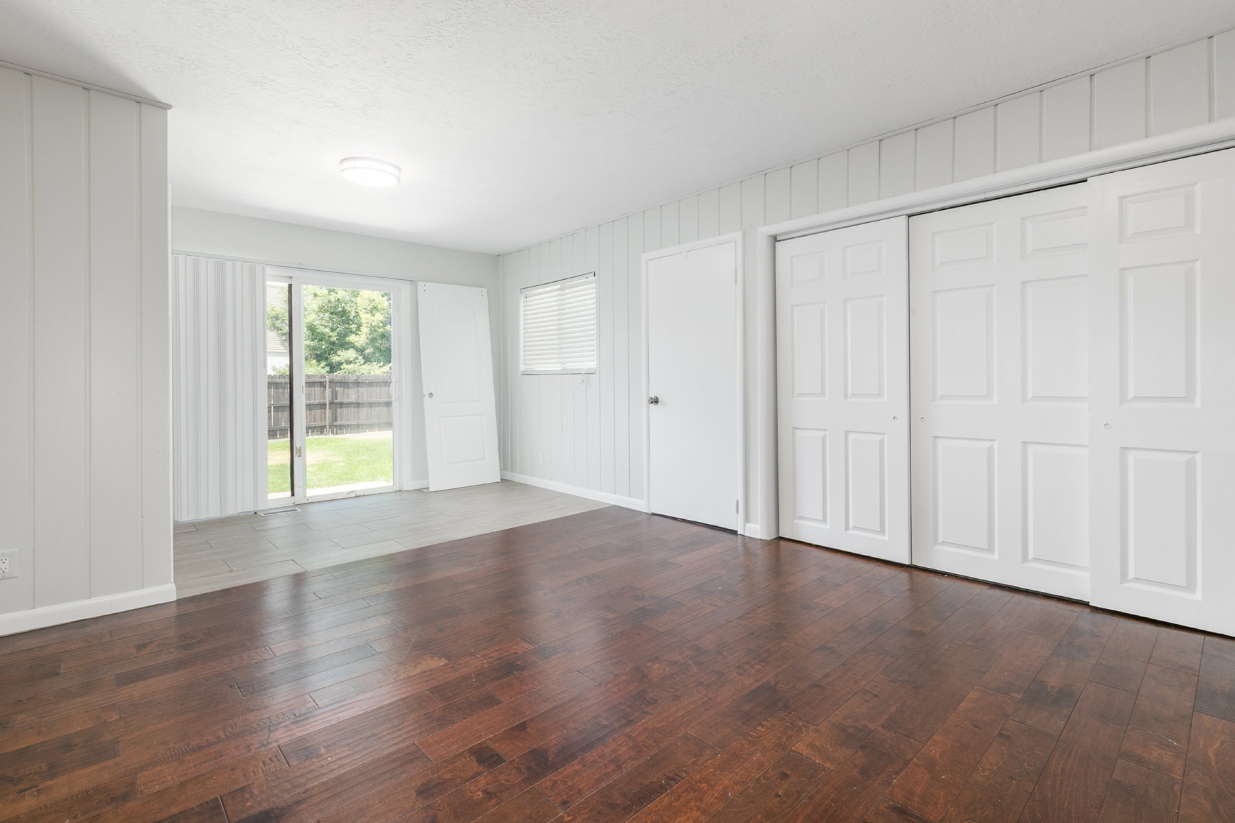 Interior space featuring rich wood-finish flooring, white paneled walls, and sliding glass doors opening to the backyard