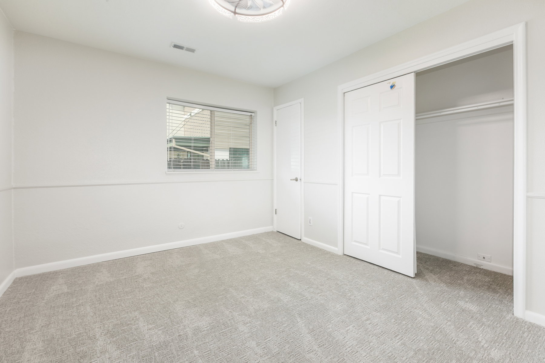 Neutral-toned room featuring light gray carpeting and white walls with wainscoting