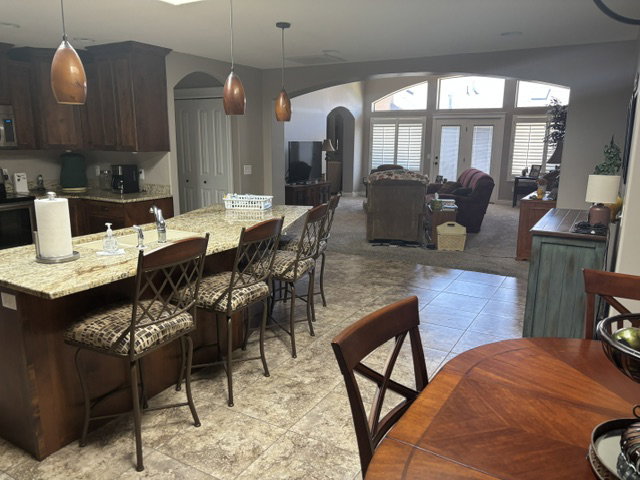 Kitchen featuring a large island with a stone countertop and seating, dark wood cabinetry, pendant lighting, and tile flooring