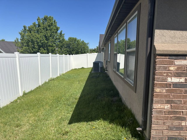 Side yard with a white vinyl privacy fence, manicured lawn, and multi-pane windows
