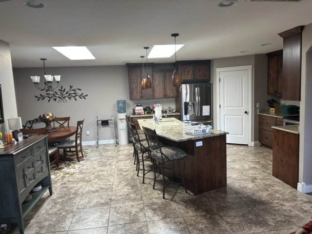 Spacious kitchen and dining area featuring skylights, recessed lighting, wood-finish cabinetry, a large kitchen island with counter seating, and patterned tile flooring