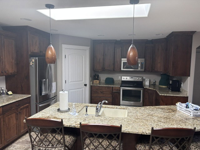 Kitchen featuring an expansive island with a light-colored sink, dark wood cabinetry, stainless steel appliances, and a rectangular skylight