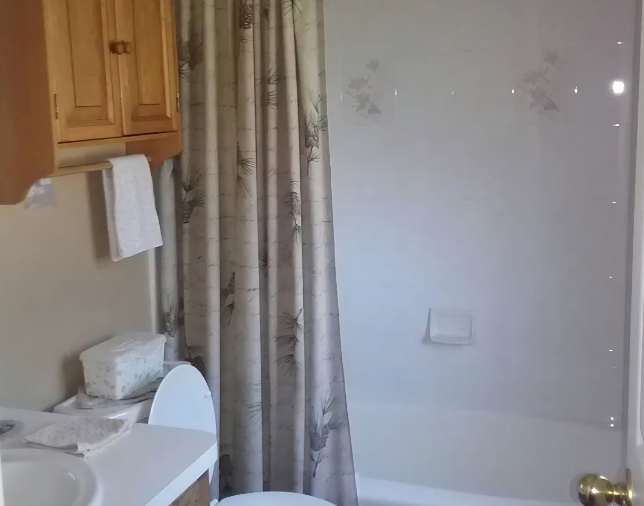 Bathroom featuring a white bathtub, a toilet, a white sink, and a wood-finish vanity with upper cabinetry