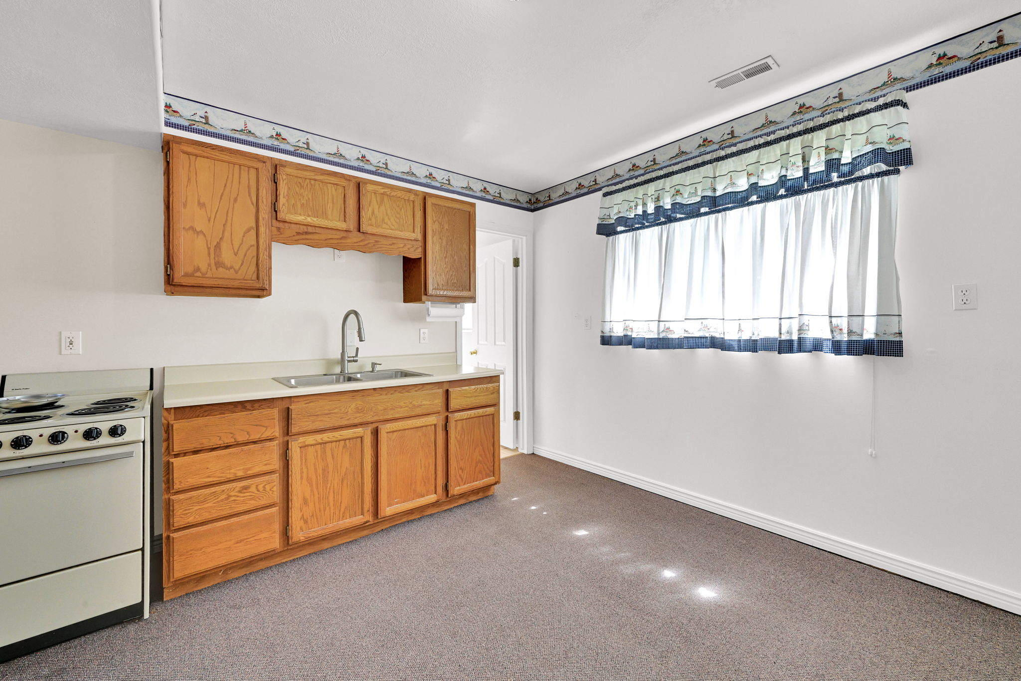 Kitchenette featuring wood-finish cabinetry, a single basin sink with a gooseneck faucet, light-toned countertops, and a white freestanding range