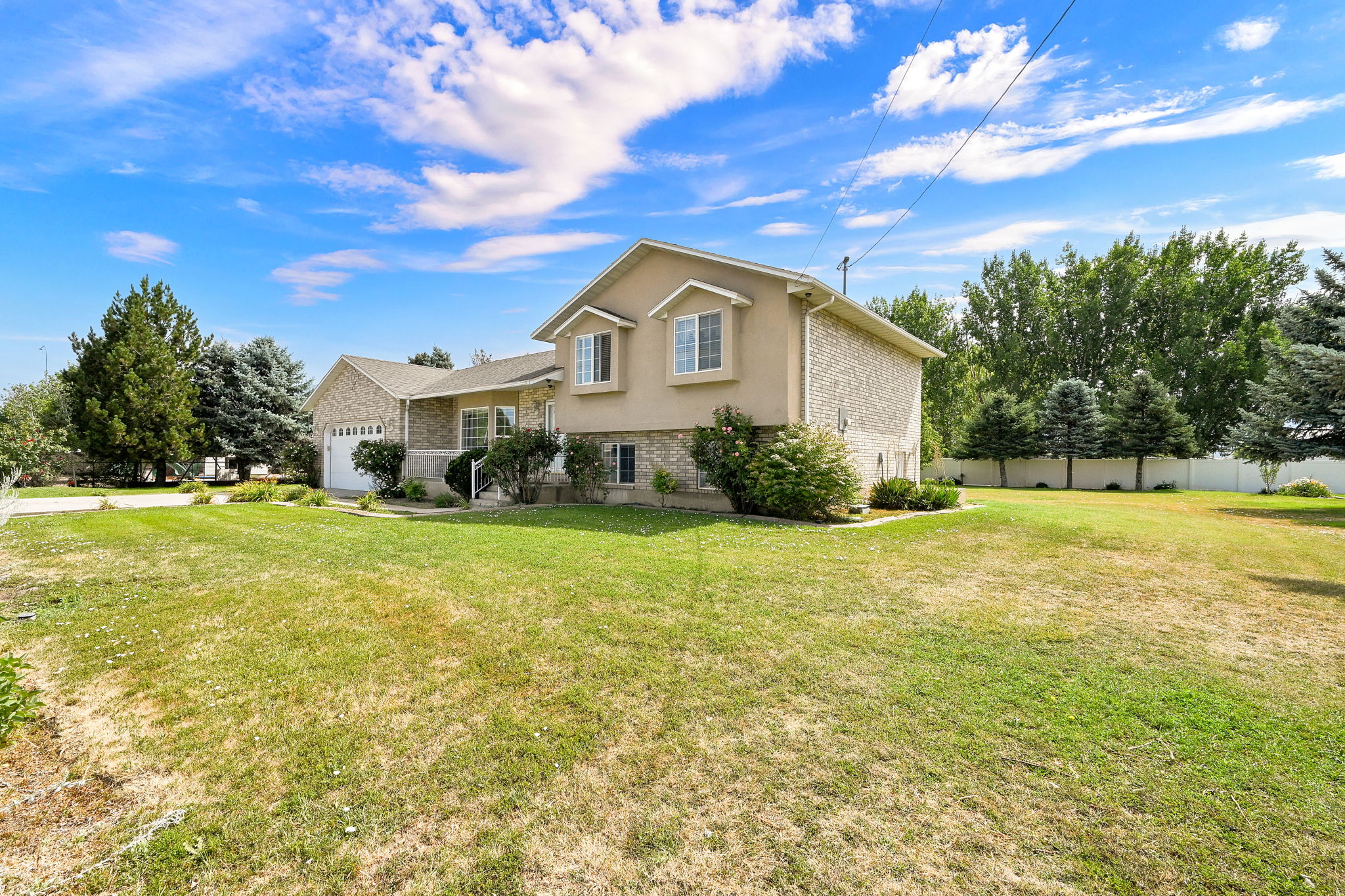 Two-story home featuring a stucco and stone exterior, an attached two-car garage, multiple windows, and a generous front lawn