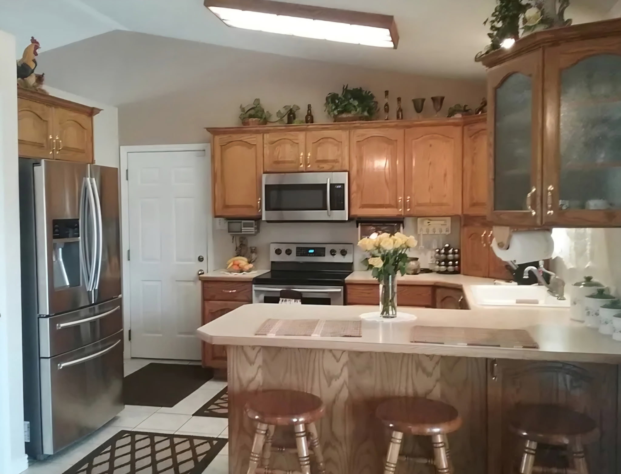 Kitchen featuring natural wood cabinetry, stainless steel appliances, a white tile floor, and a breakfast bar with a light-colored countertop