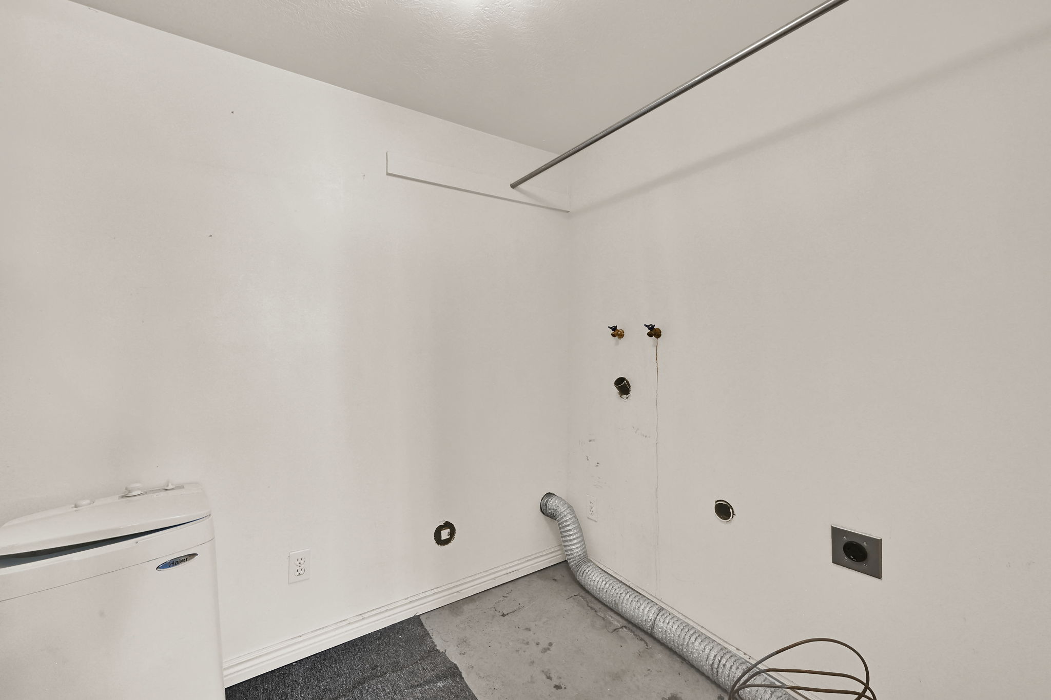 Dedicated laundry area featuring white walls, baseboards, and a concrete floor